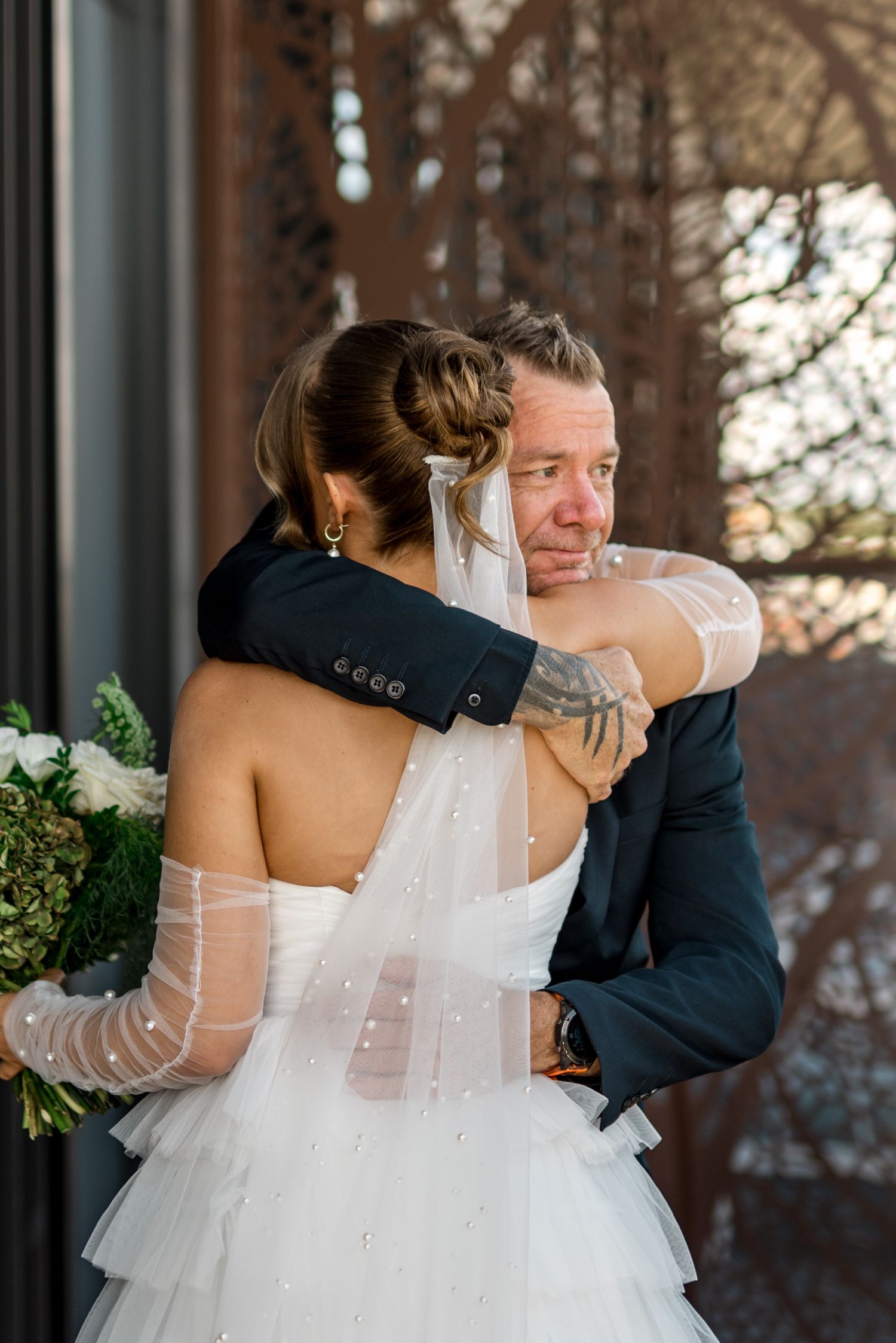 Tearful groom hugs bride in tiered white gown during emotional first look at wedding.