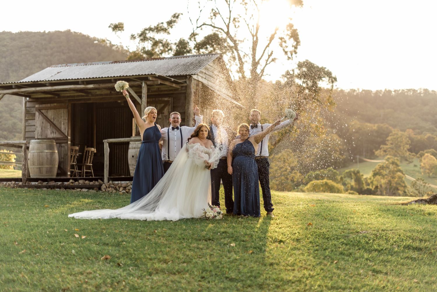 Wedding party celebrates with confetti outside a rustic barn at a stunning farm wedding venue.