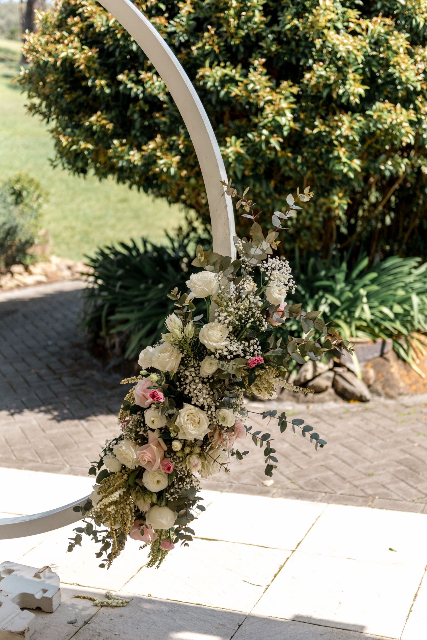 Elegant wedding arch adorned with white and pink roses, baby's breath, and eucalyptus greenery at an outdoor ceremony.