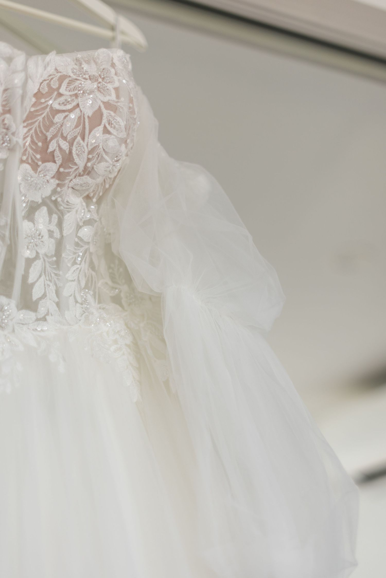 Elegant white lace wedding dress with floral embroidery and tulle sleeves hanging on a hanger.