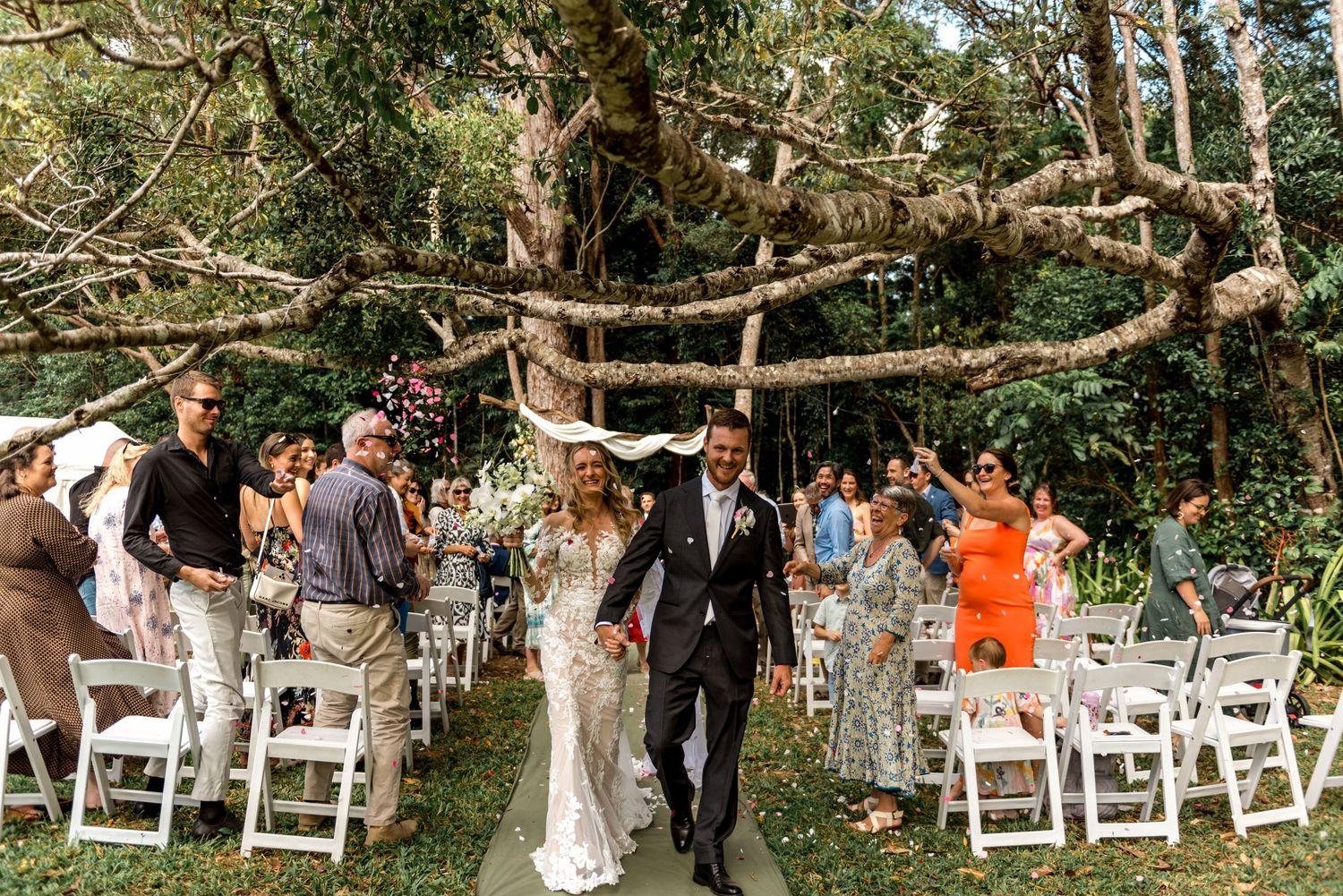 Happy newlyweds walk hand in hand down aisle after outdoor forest wedding ceremony.