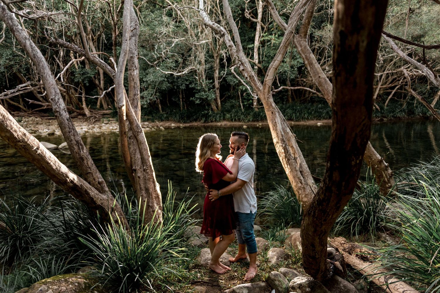 Romantic couple embracing among twisted trees beside a tranquil forest creek in natural light.