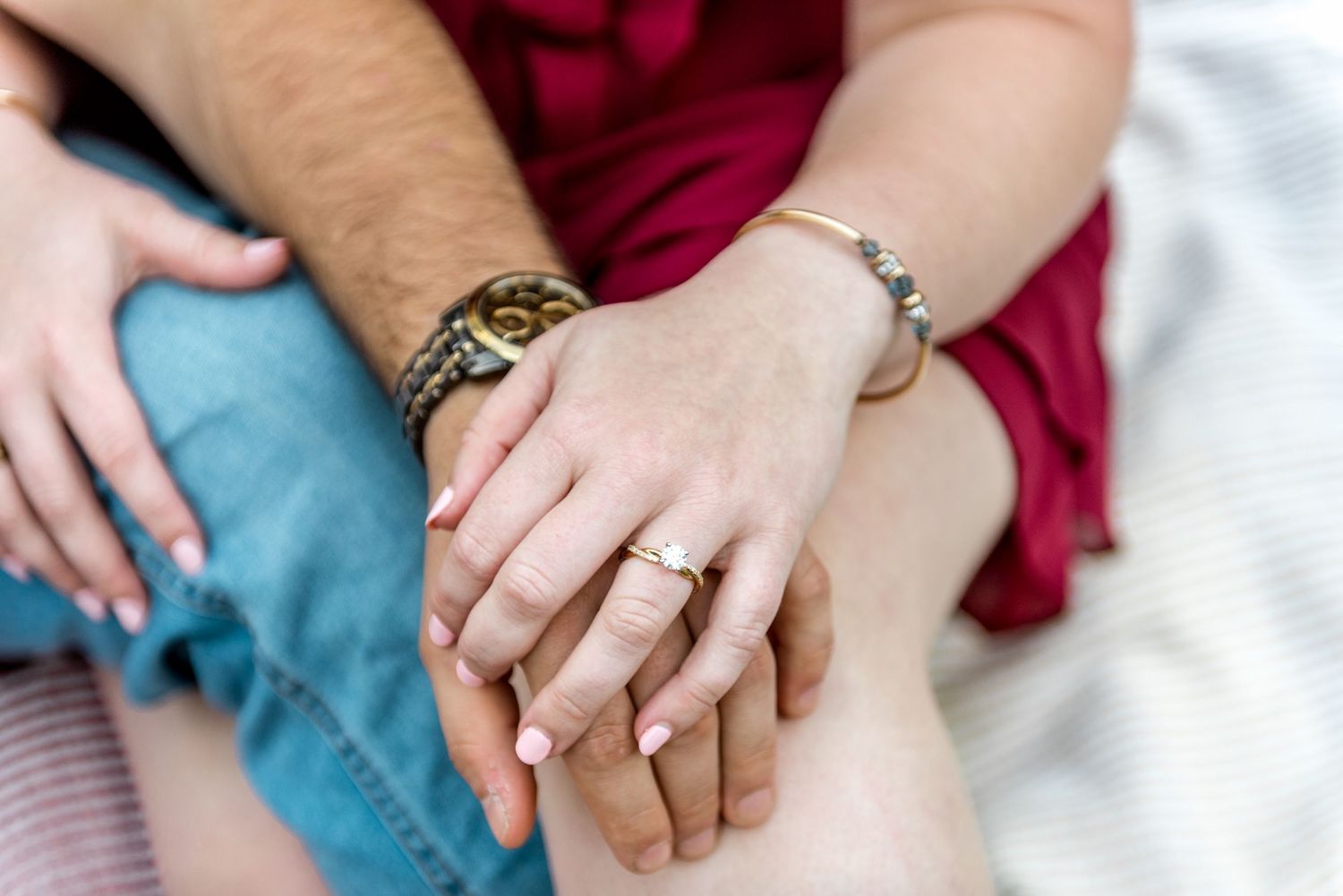 Close-up of an engaged couple holding hands, showing a diamond ring, watch, and bracelet.