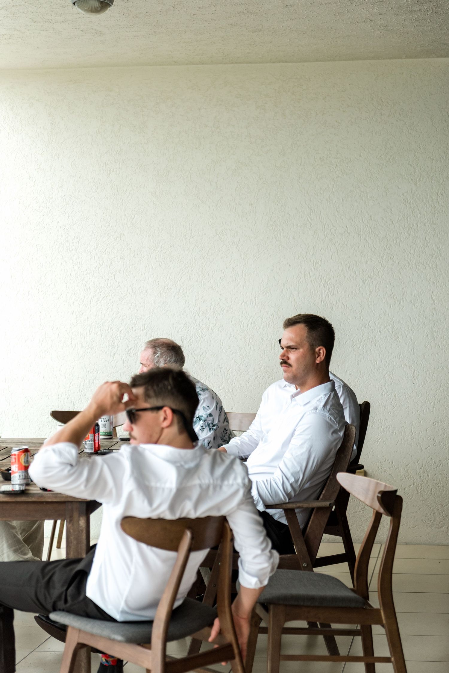Groomsmen in white shirts relaxing casually at a dining table during wedding preparations.