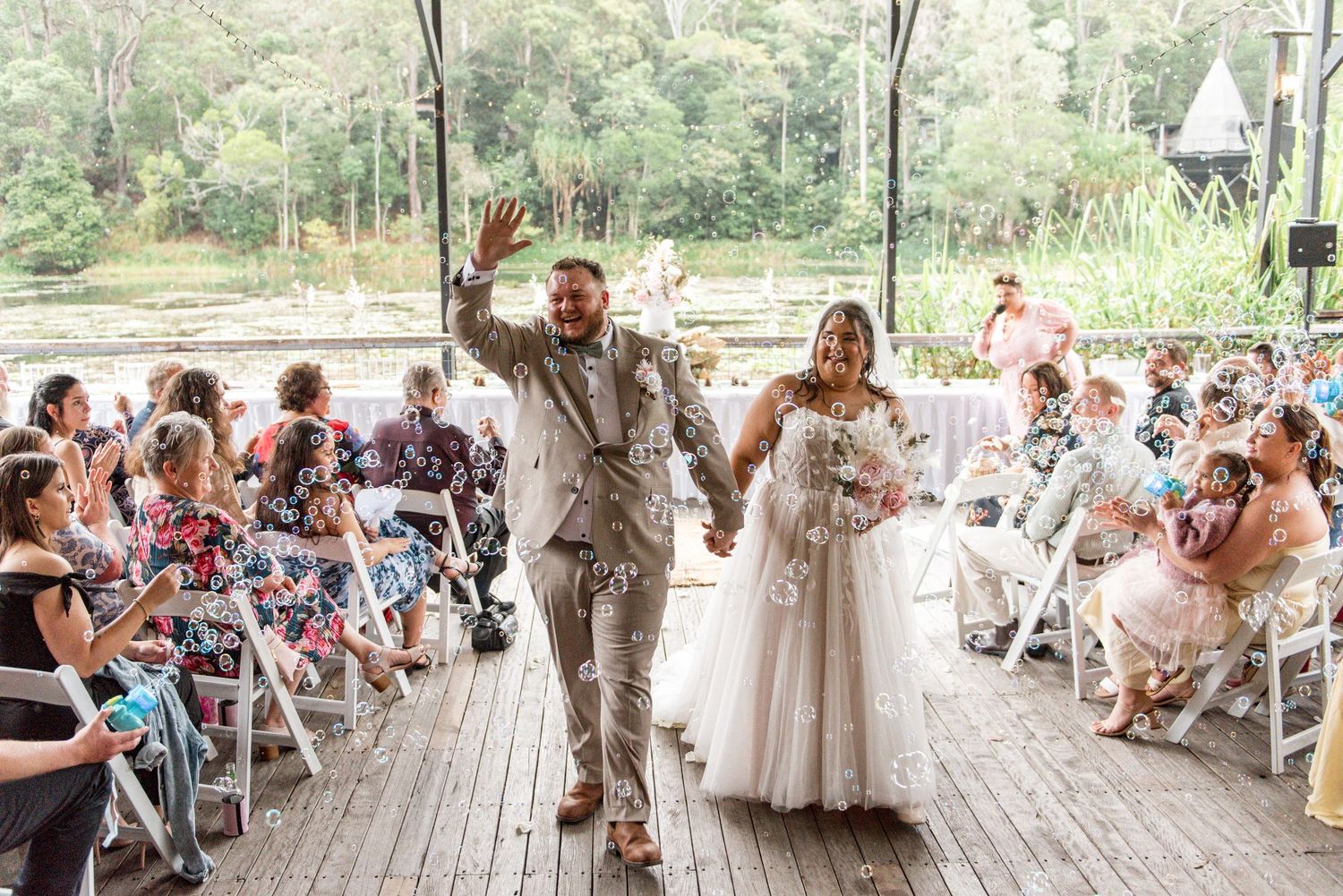 Newlyweds walk back down the aisle celebrating as guests cheer at an outdoor wedding ceremony.