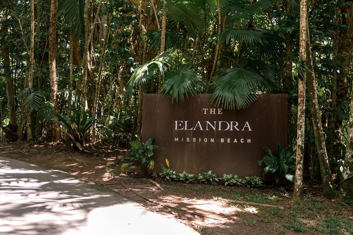 Elegant wooden entrance sign for The Elandra Mission Beach resort surrounded by lush tropical rainforest.