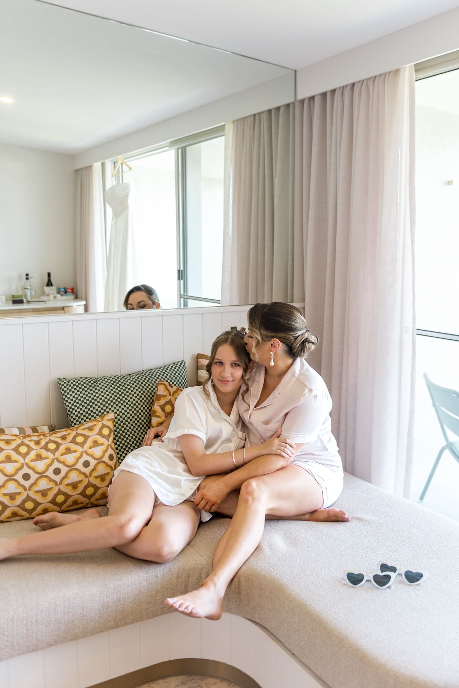 Bride and bridesmaid sharing a tender embrace on a couch during pre-wedding getting ready moments.