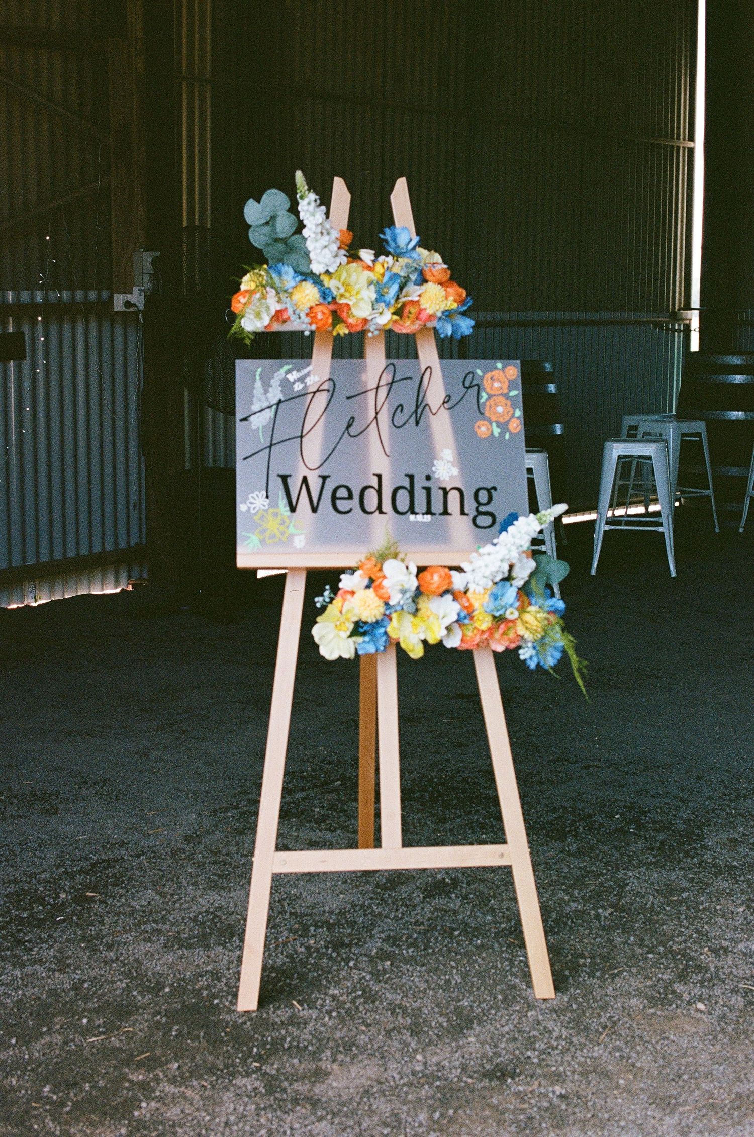 Fletcher Wedding welcome sign decorated with colorful orange blue and yellow flowers on wooden easel.