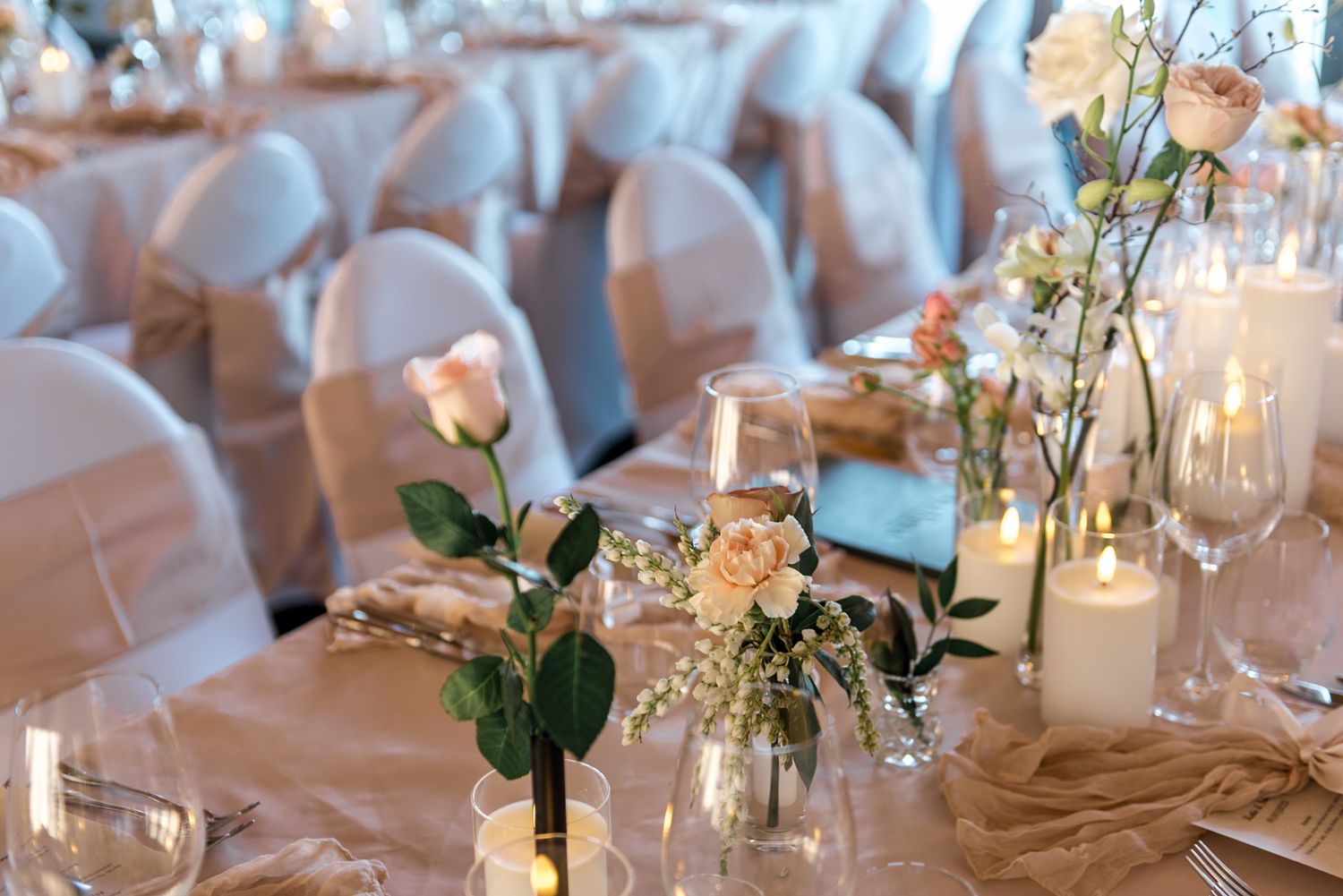 Wedding reception table with single stem roses, small floral arrangements, candles, and crystal wine glasses.