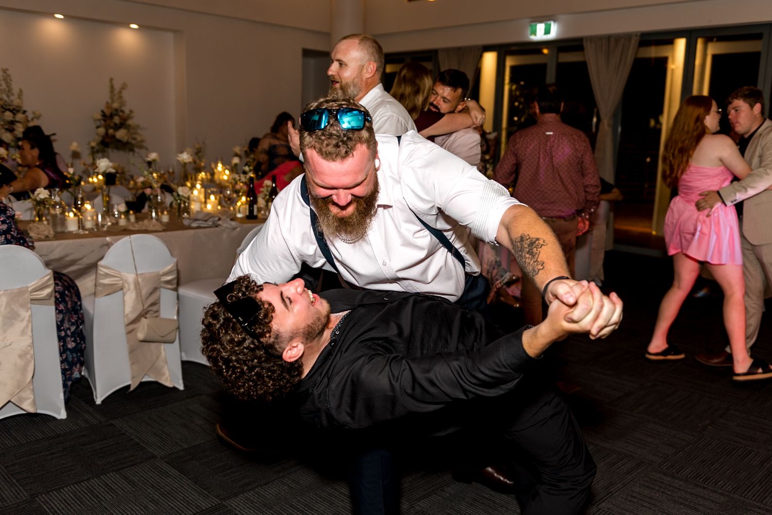 Bearded groomsman dramatically dips a guest on the wedding dance floor.