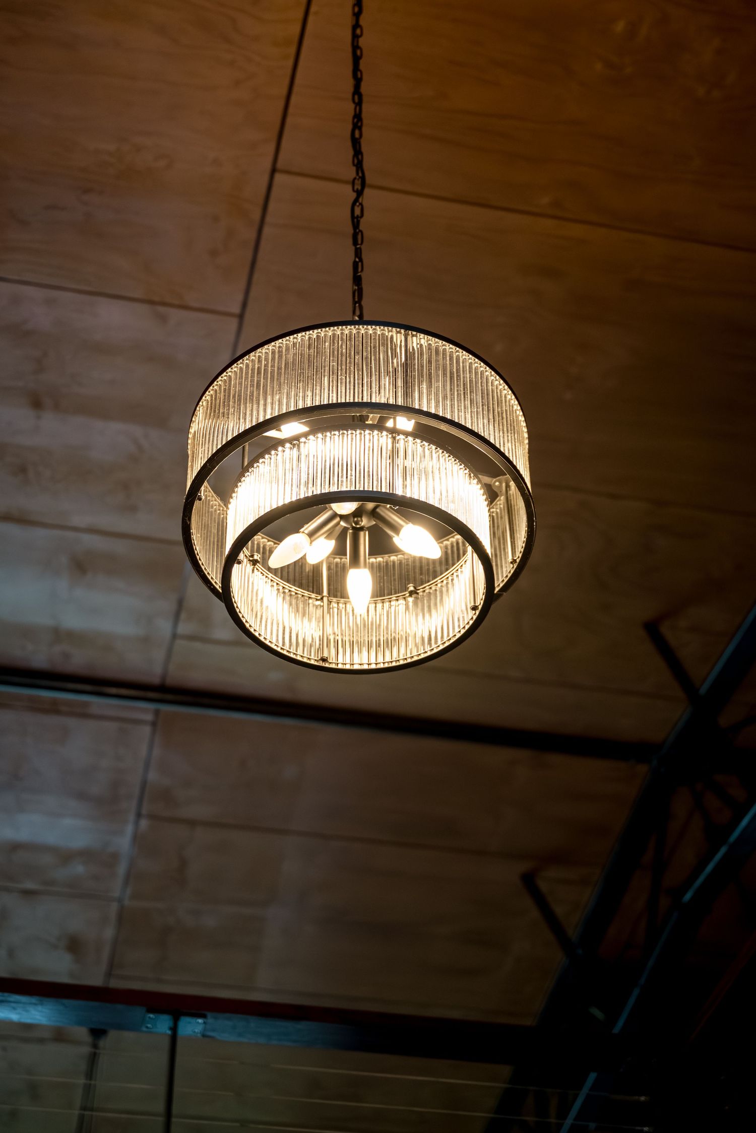 Elegant tiered glass chandelier hanging from wooden ceiling with warm glowing bulbs.