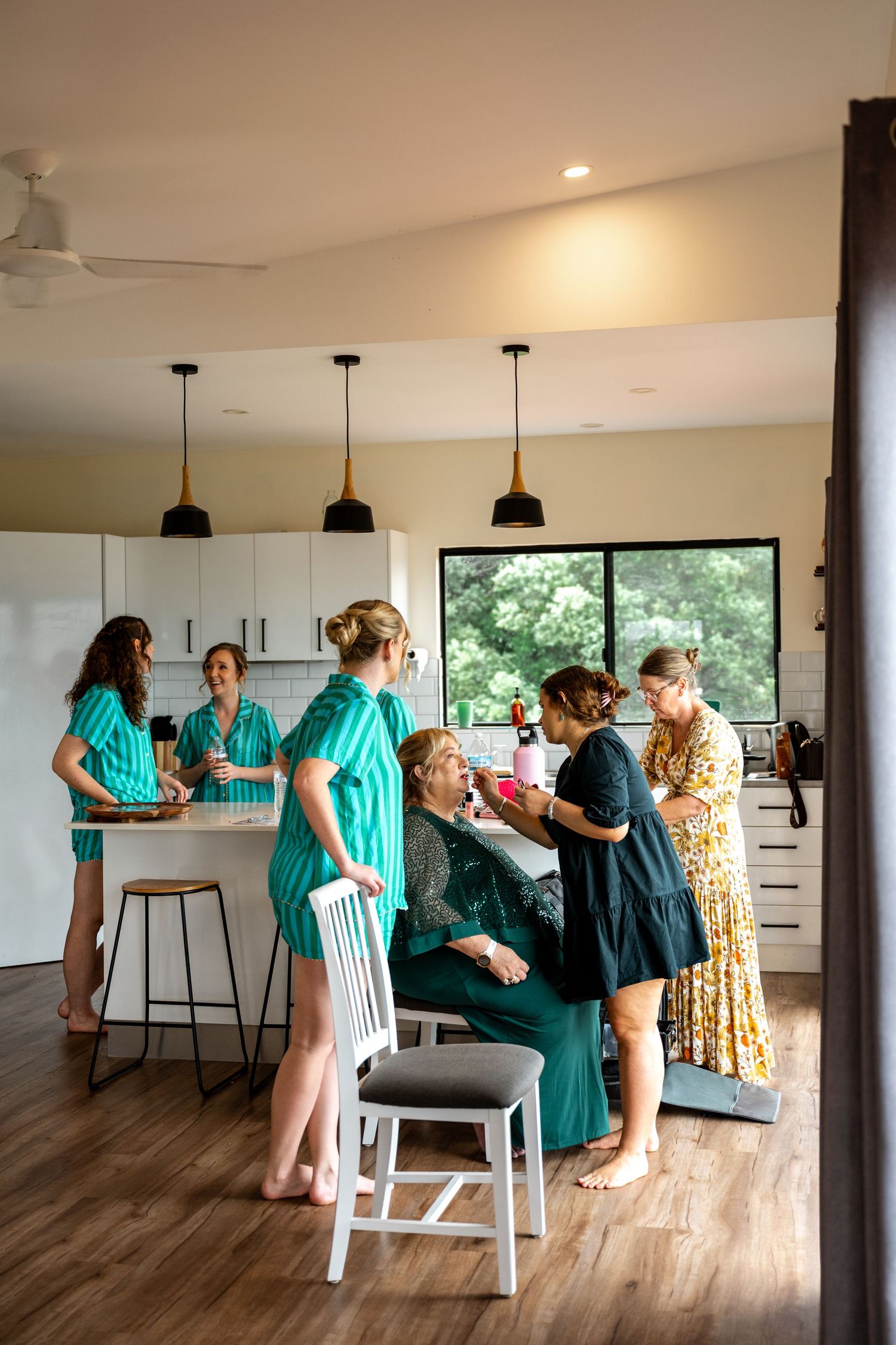Bridal party in teal robes gathered in modern kitchen during wedding morning preparations.