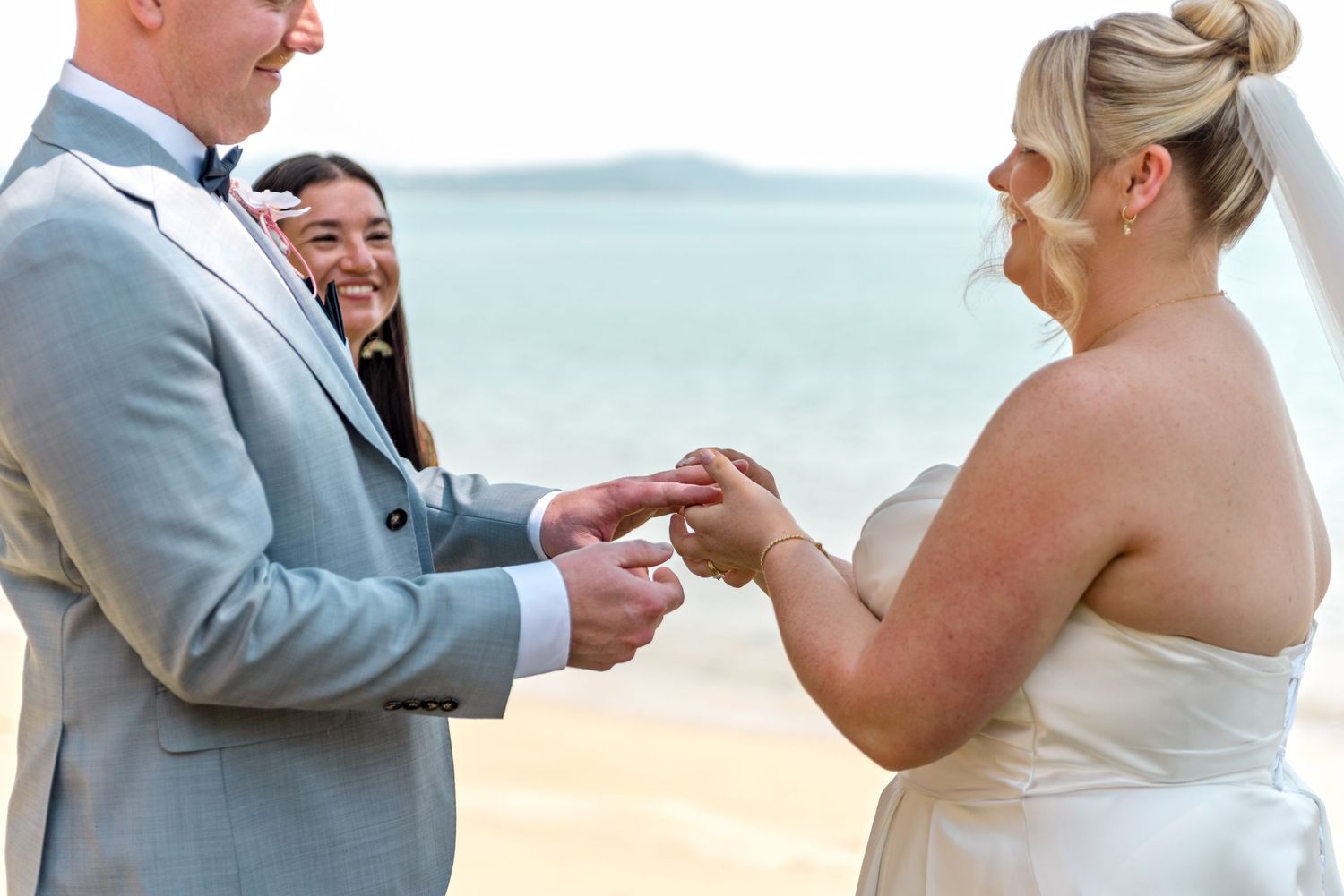 Bride and groom exchanging rings at outdoor beach wedding ceremony.