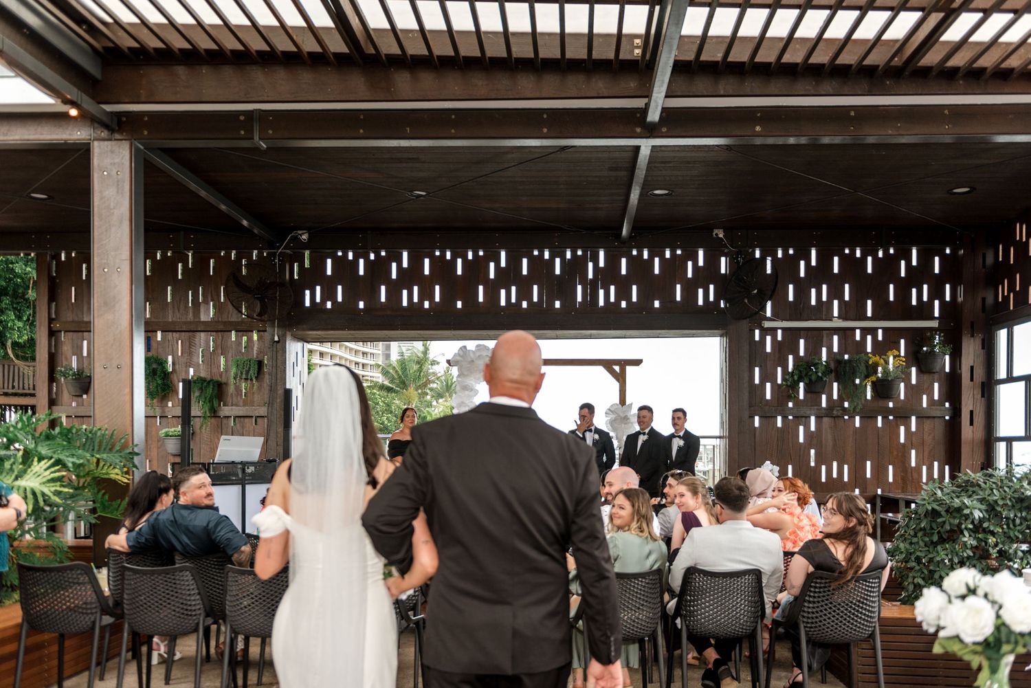Bride and escort walk down aisle at modern open-air wedding ceremony venue.