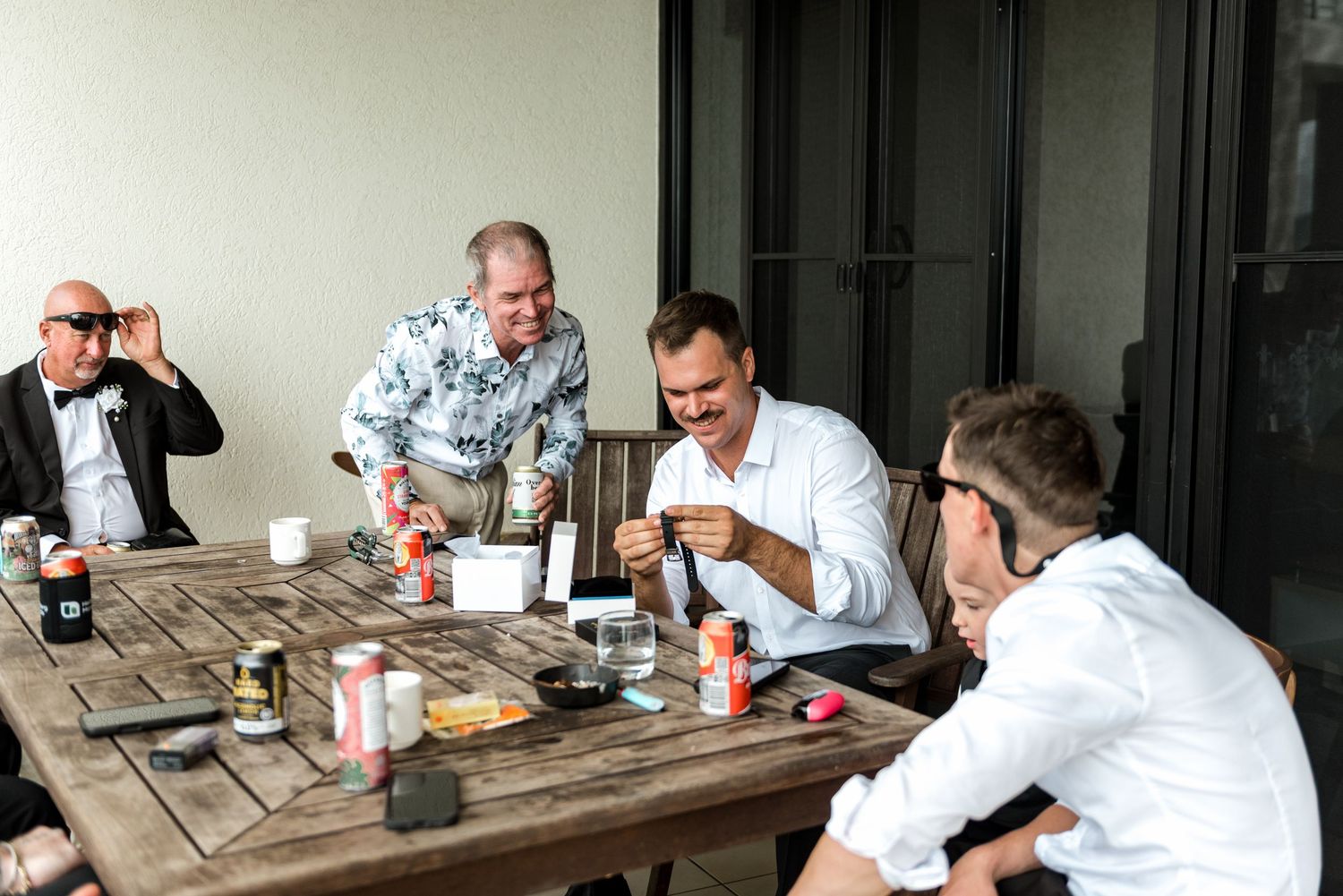 Groomsmen relaxing and laughing together around a wooden table on an outdoor patio.