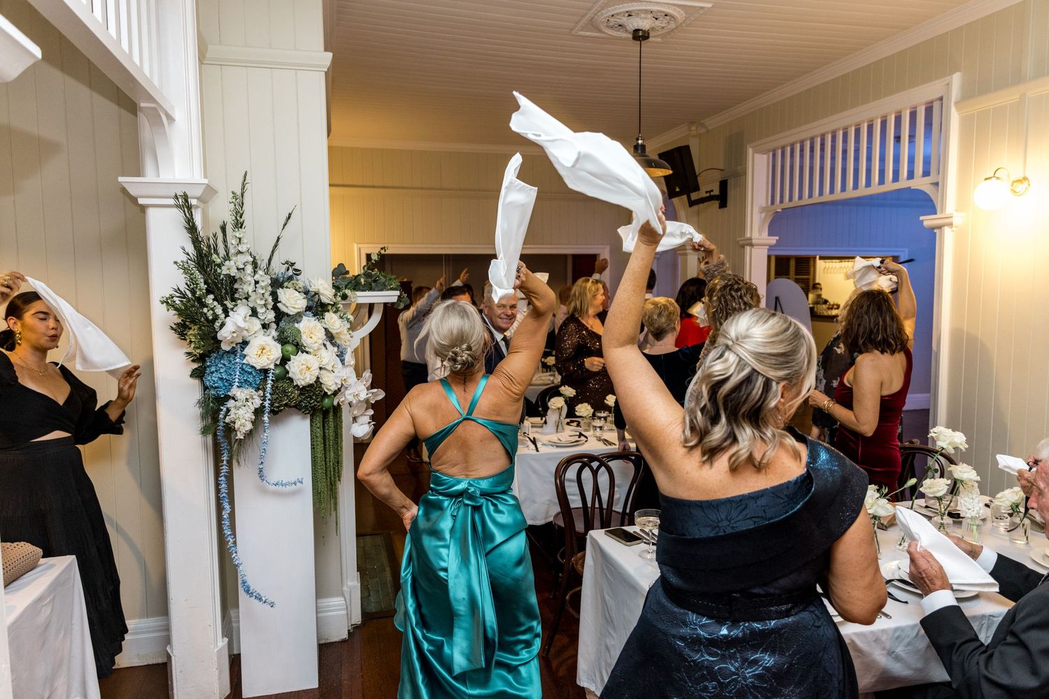 Wedding guests in formal attire waving white napkins during a lively reception celebration.