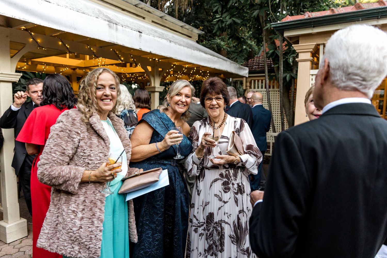 Wedding guests socializing and smiling outdoors at an elegant evening garden reception.
