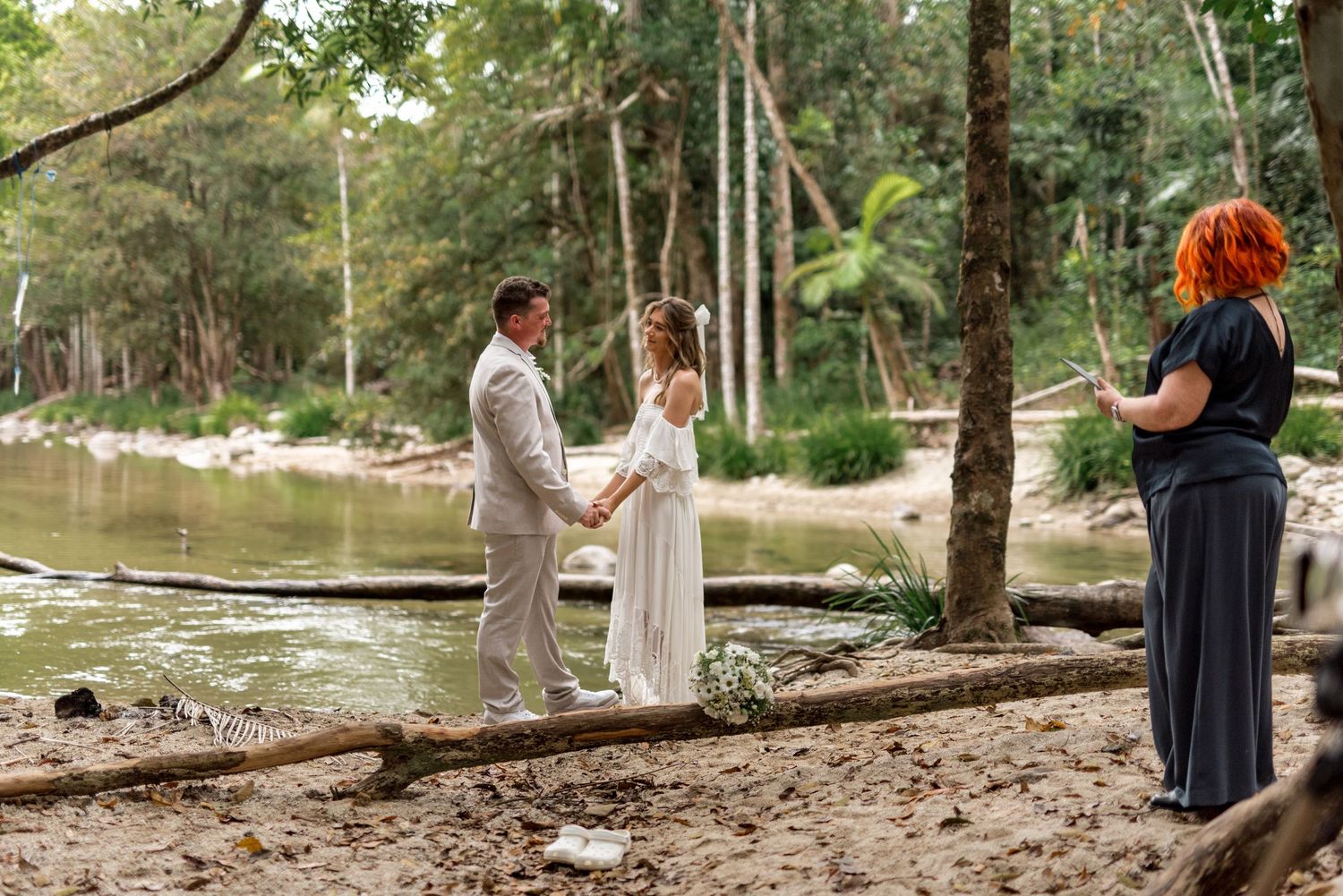 Couple holds hands during intimate elopement ceremony beside a peaceful rainforest creek.