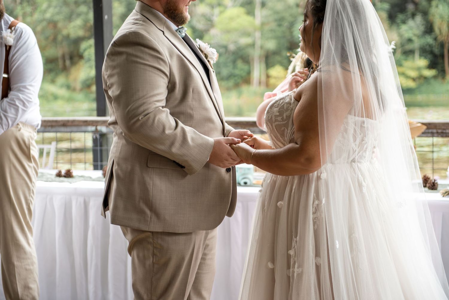 Bride and groom exchange rings during intimate outdoor wedding ceremony by a pond.