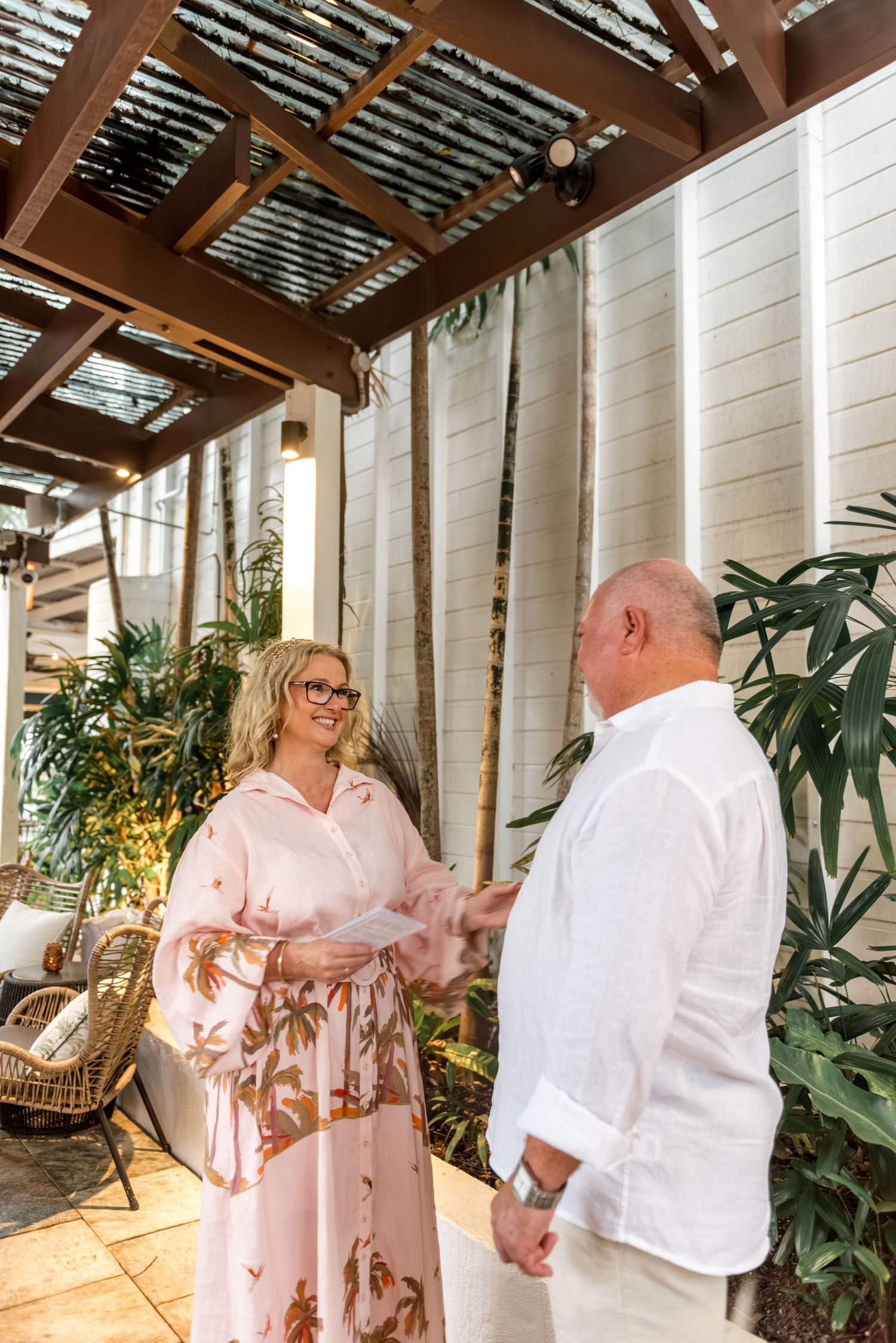 Happy couple holding hands and smiling during intimate outdoor wedding ceremony under pergola.