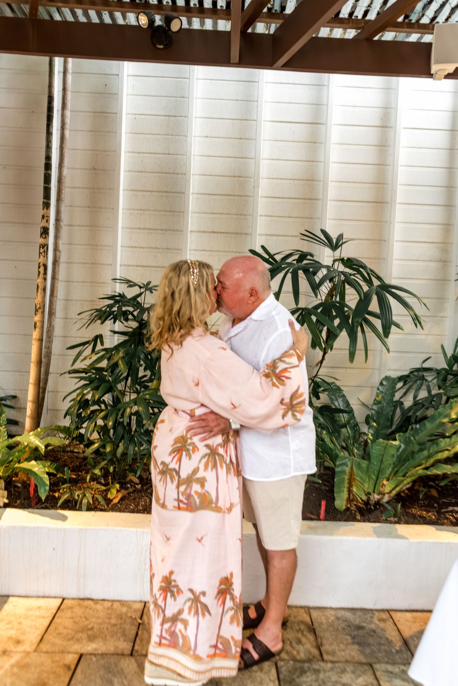 Couple sharing first kiss as newlyweds surrounded by lush tropical garden greenery.