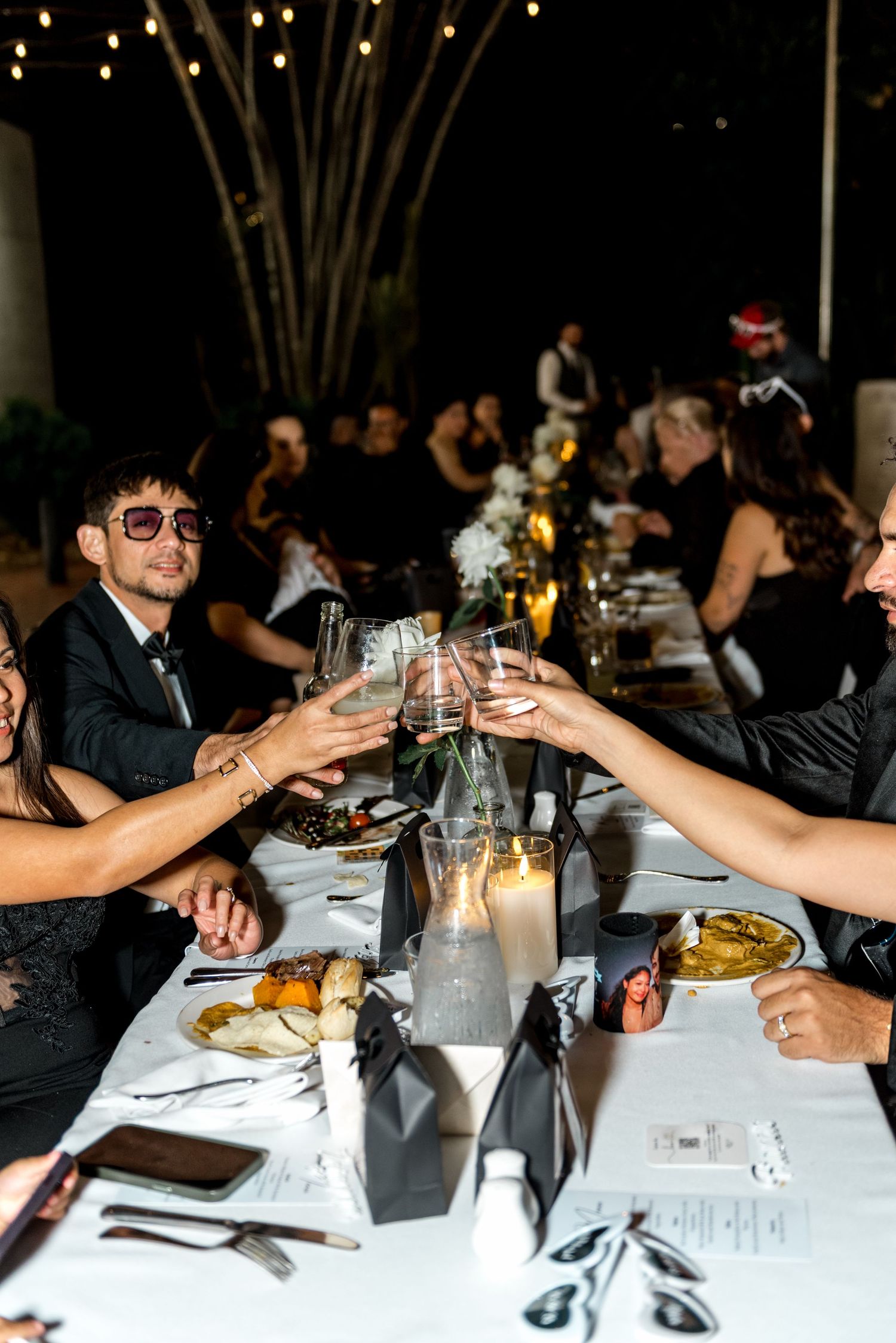 Wedding guests raise glasses in a toast at a candlelit reception dinner table decorated in black and white.