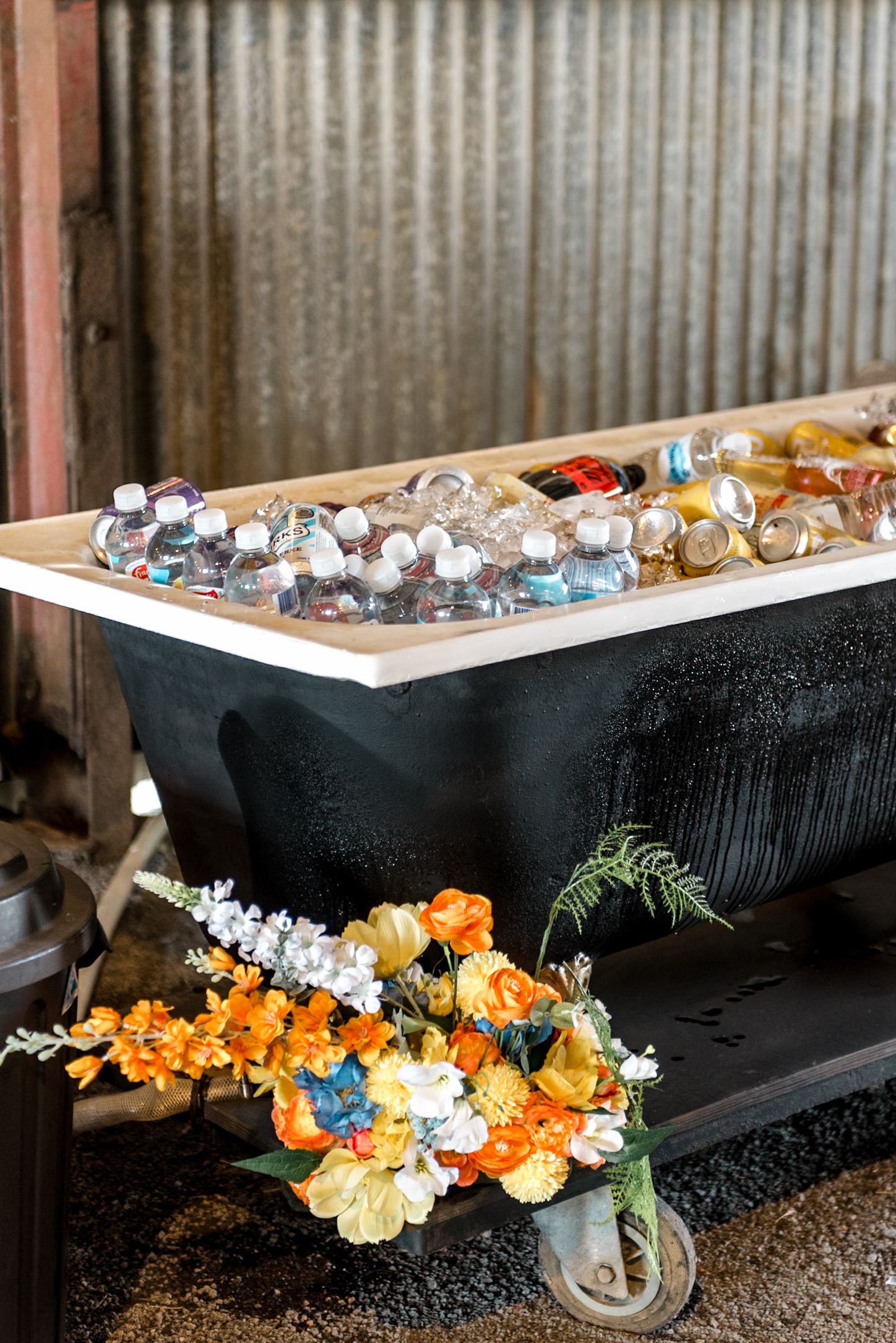 Vintage black bathtub filled with ice and bottled drinks decorated with colorful flowers.