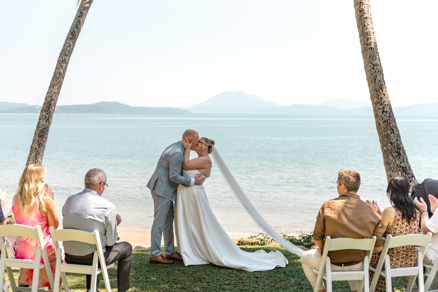 Couple sharing first kiss at tropical beachside wedding ceremony.