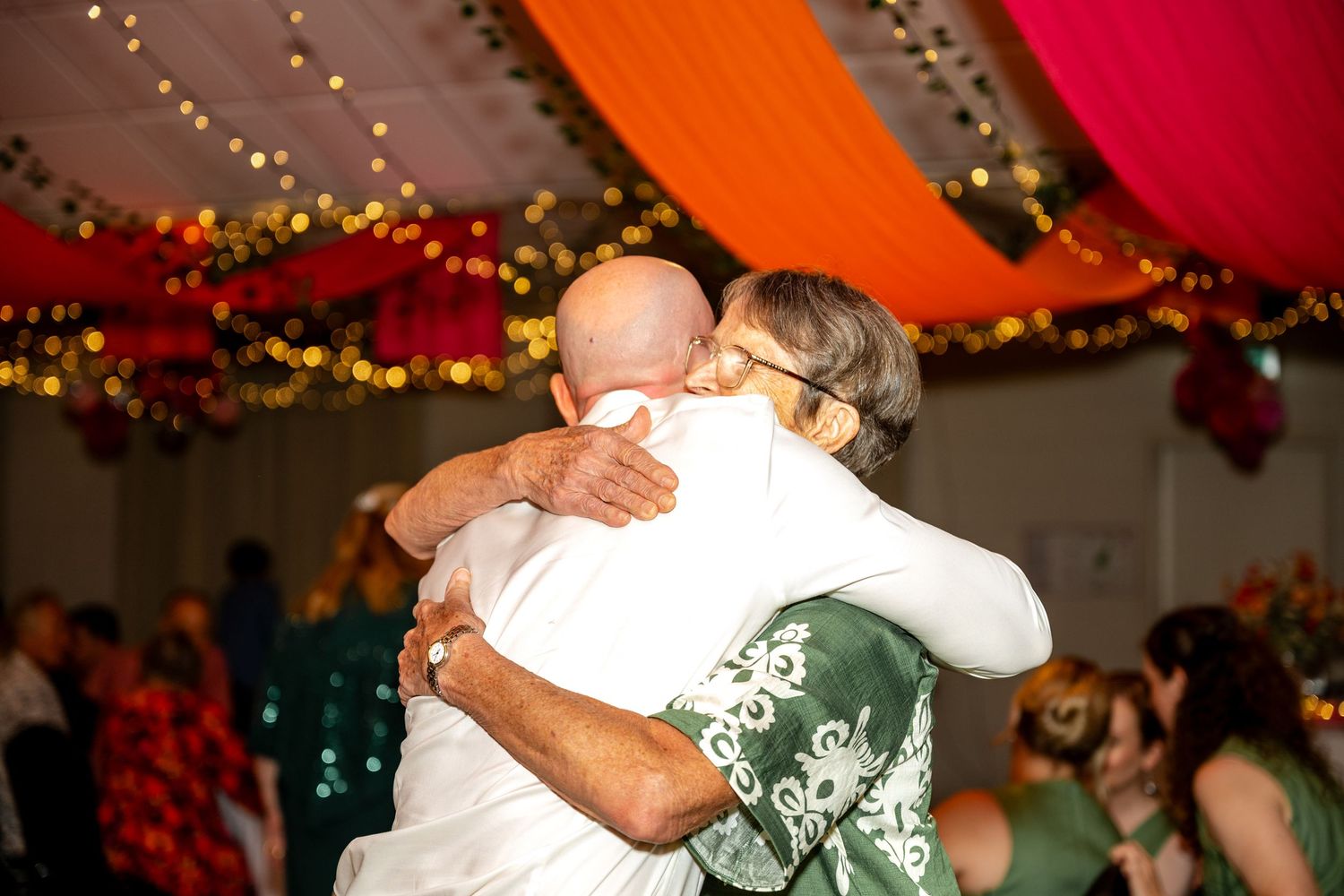 Two guests sharing a warm embrace on the dance floor at a colorfully decorated wedding reception.