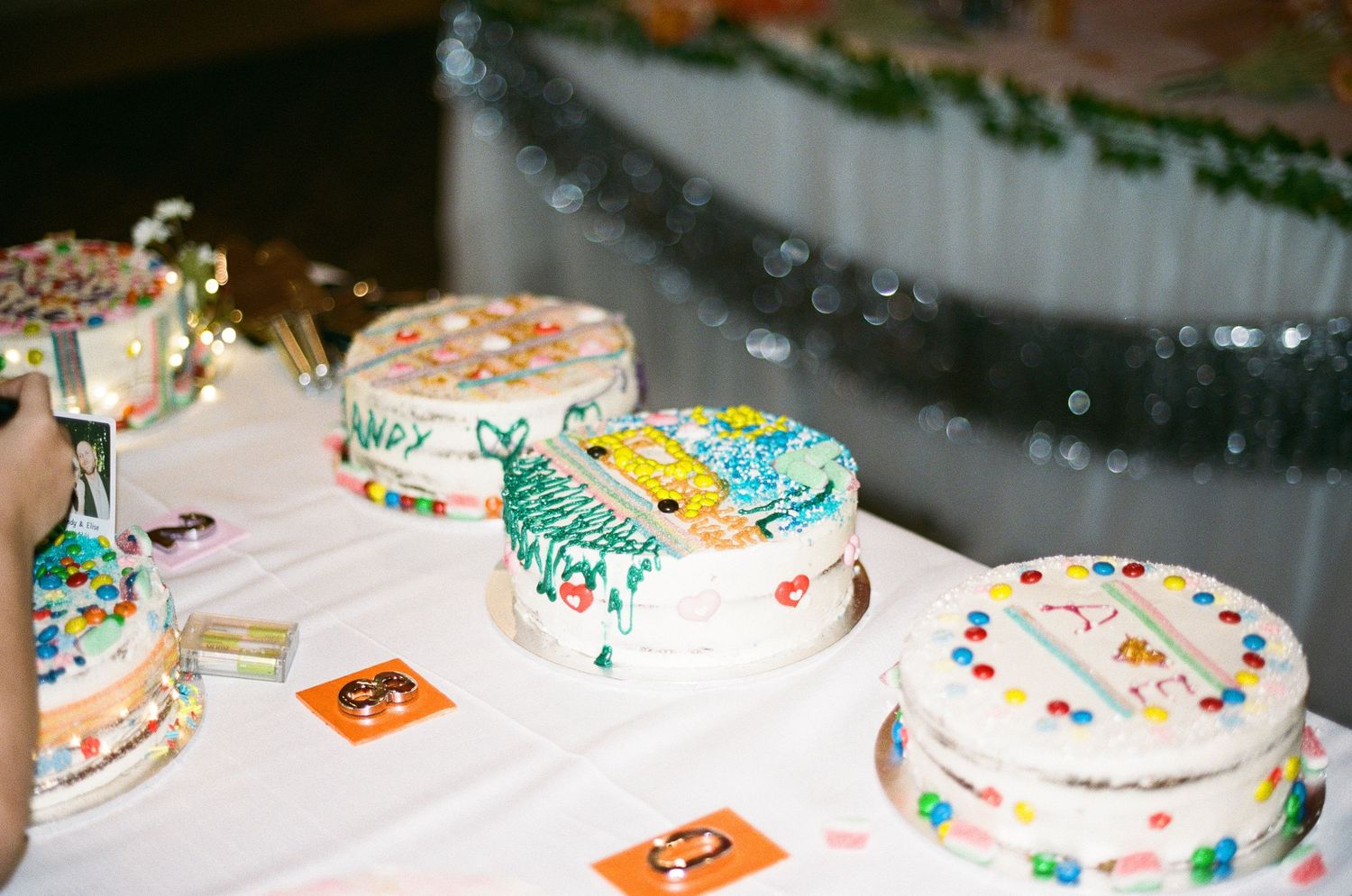 Colorful decorated wedding cakes displayed on a white tablecloth at a festive reception table.