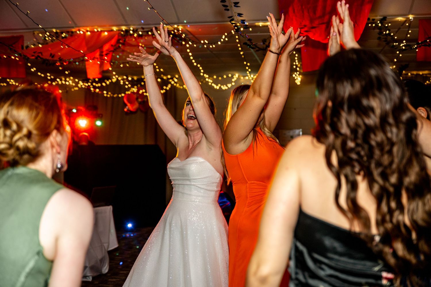 Bride and guests raising hands on the dance floor at a wedding reception.