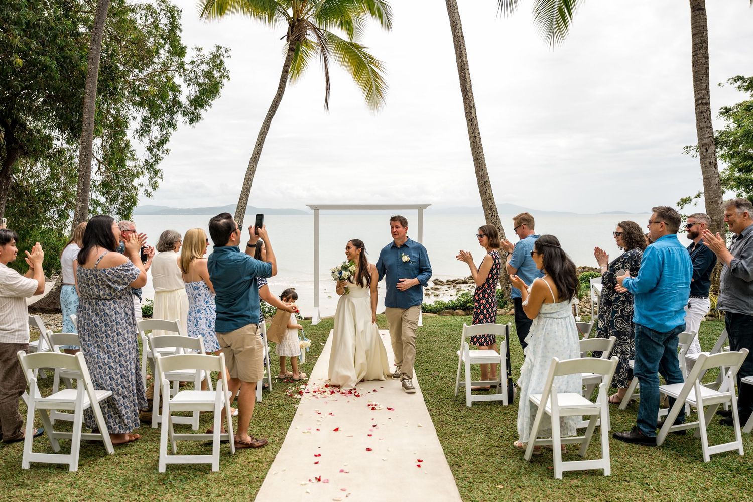 Newlyweds at the altar of a tropical outdoor wedding ceremony with guests applauding at Little Cove, Port Douglas.