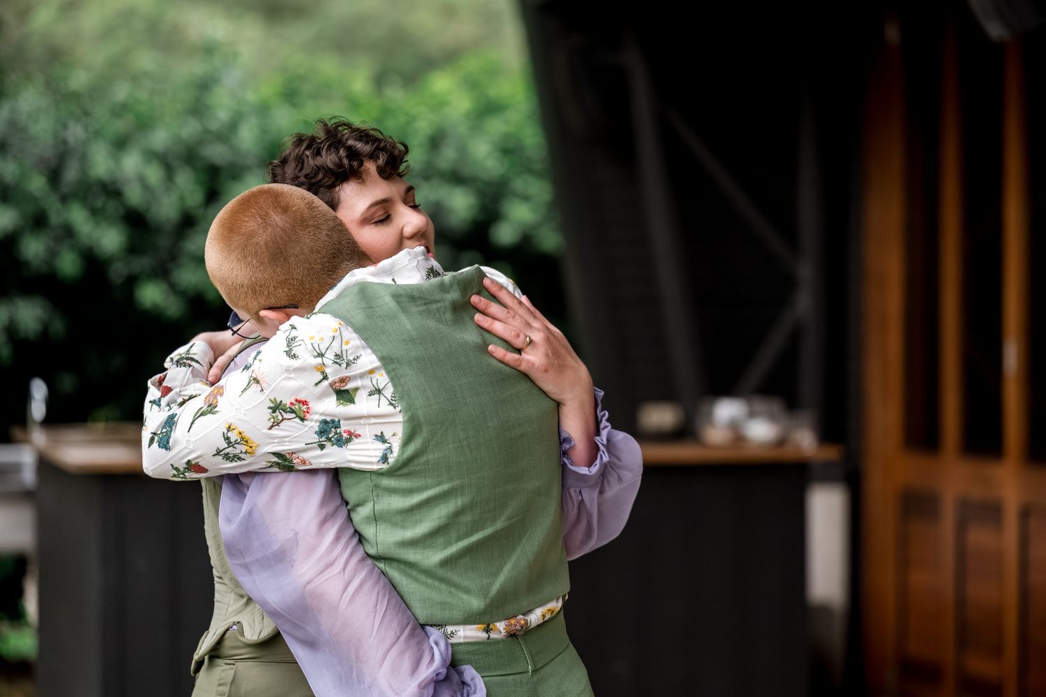Two people share a warm embrace outdoors at a wedding celebration.
