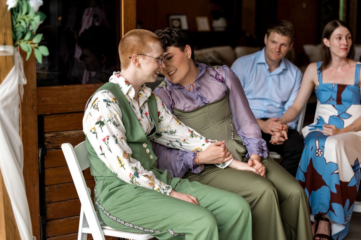 Two people in green outfits hold hands intimately during a wedding ceremony while guests watch.