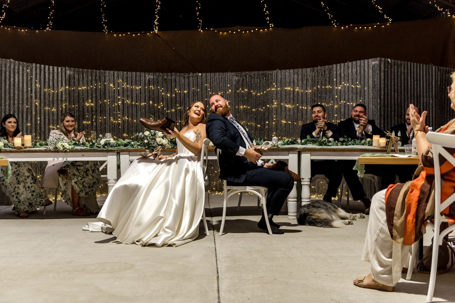 Bride and groom share a joyful moment at sweetheart table during rustic barn wedding reception.
