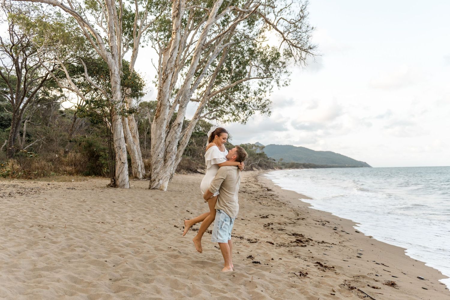 A couple shares a romantic moment as the man lifts the woman on a scenic sandy beach.