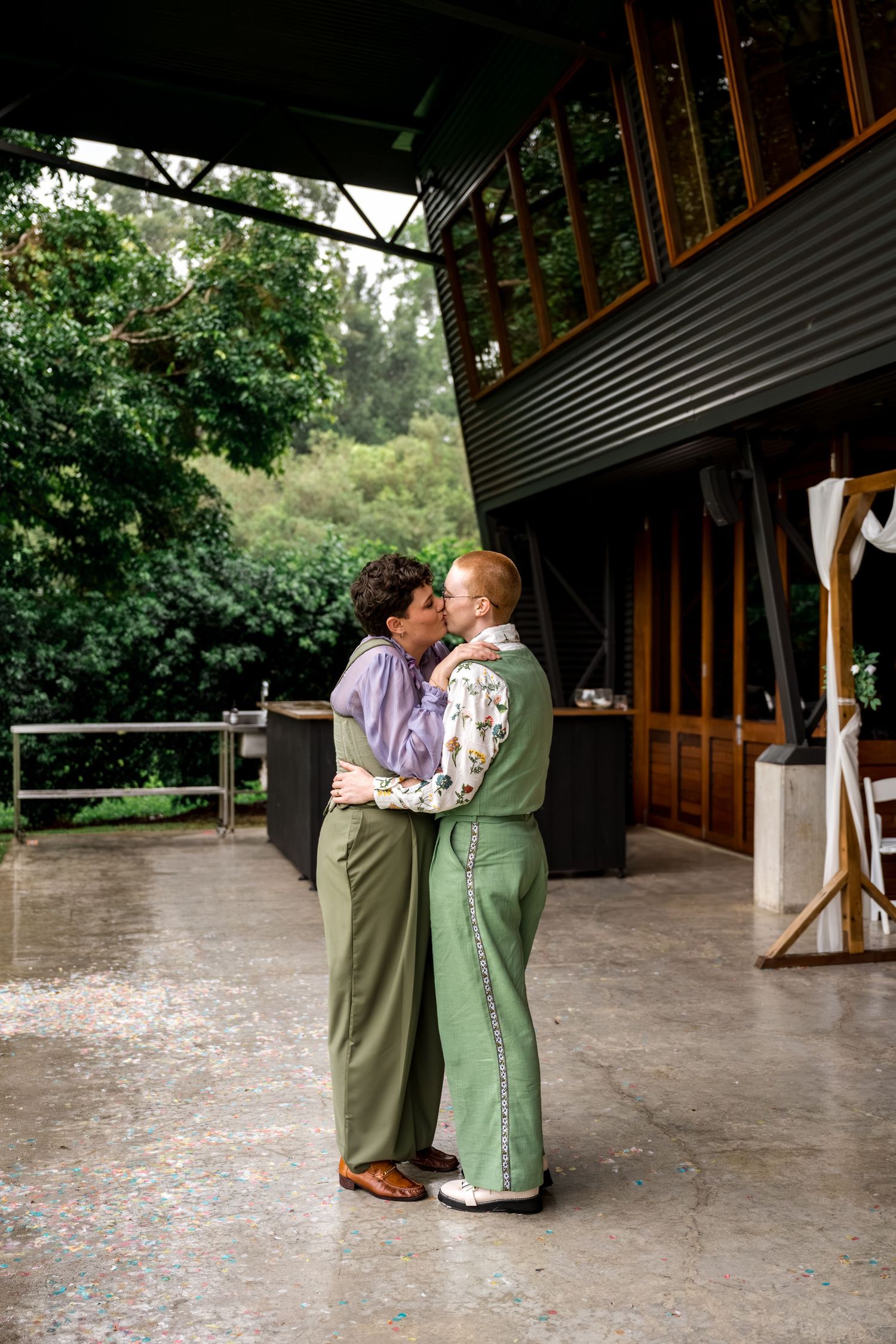 Couple in green outfits sharing a romantic kiss on a covered outdoor concrete patio.