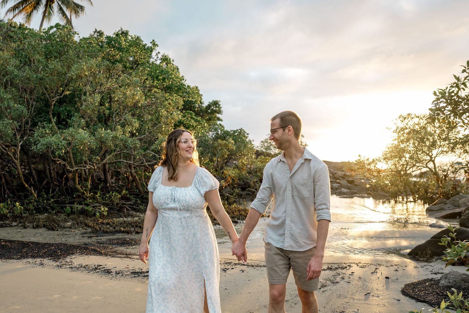 Happy couple holding hands and smiling at each other on sandy beach at warm tropical sunset at Four Mile Beach, Port Douglas.
