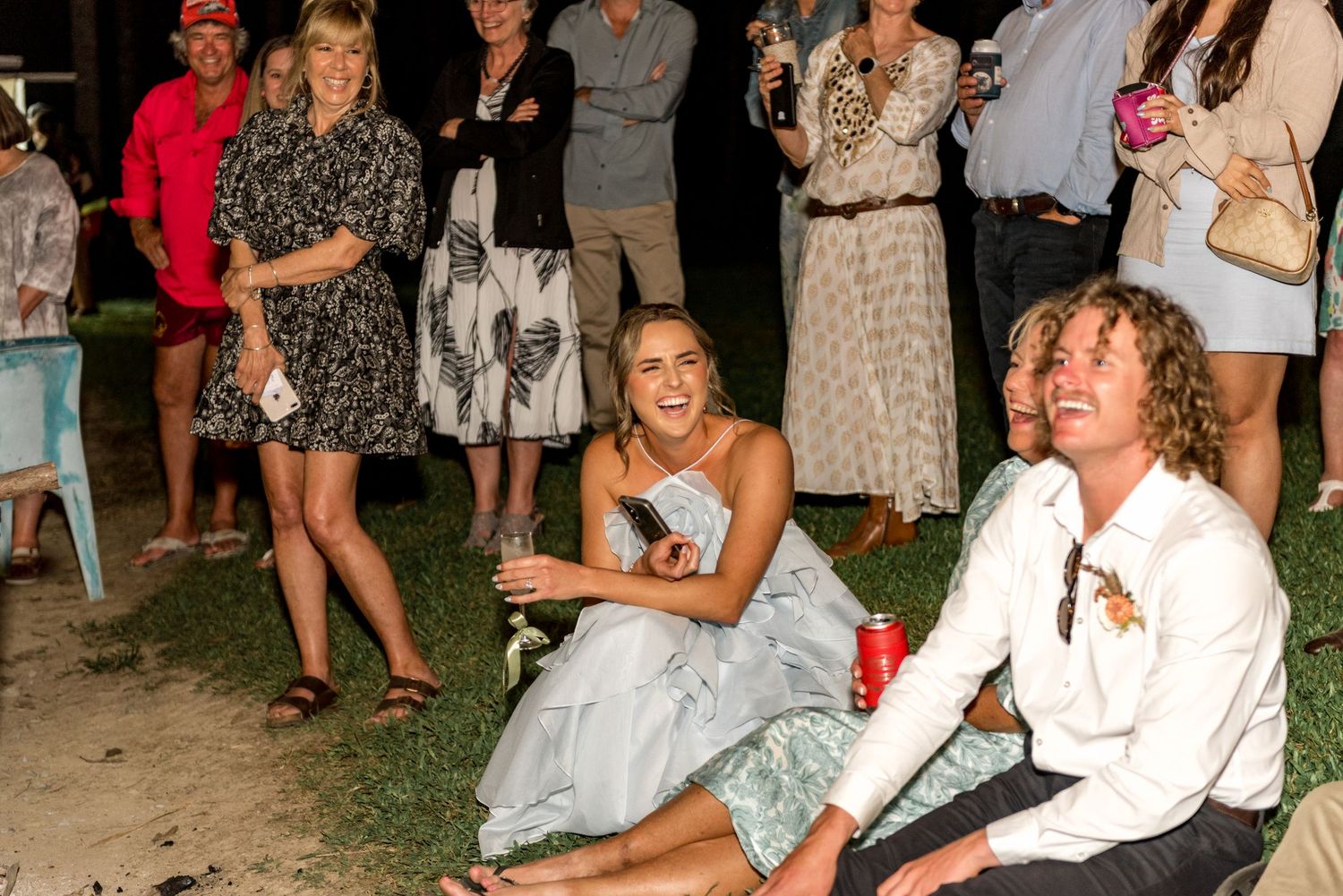 Bride laughing joyfully with guests at outdoor nighttime wedding reception celebration.