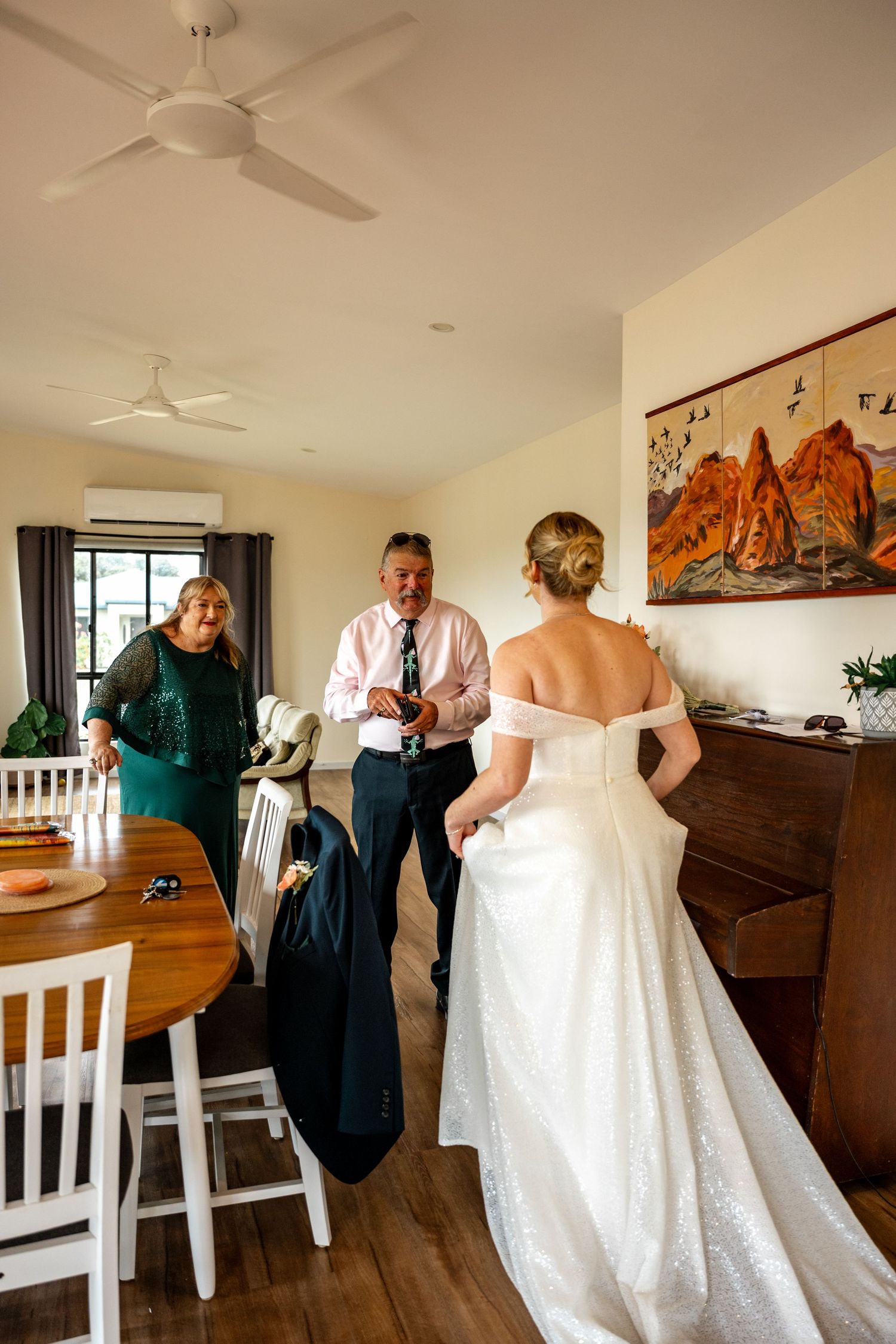 Bride in white gown meets parents during wedding morning preparations in a cozy home interior.