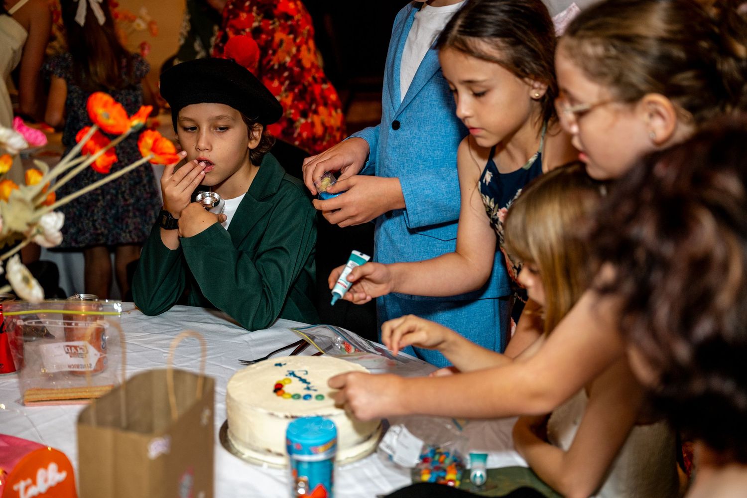 Children decorate a white cake together at a festive wedding reception table.