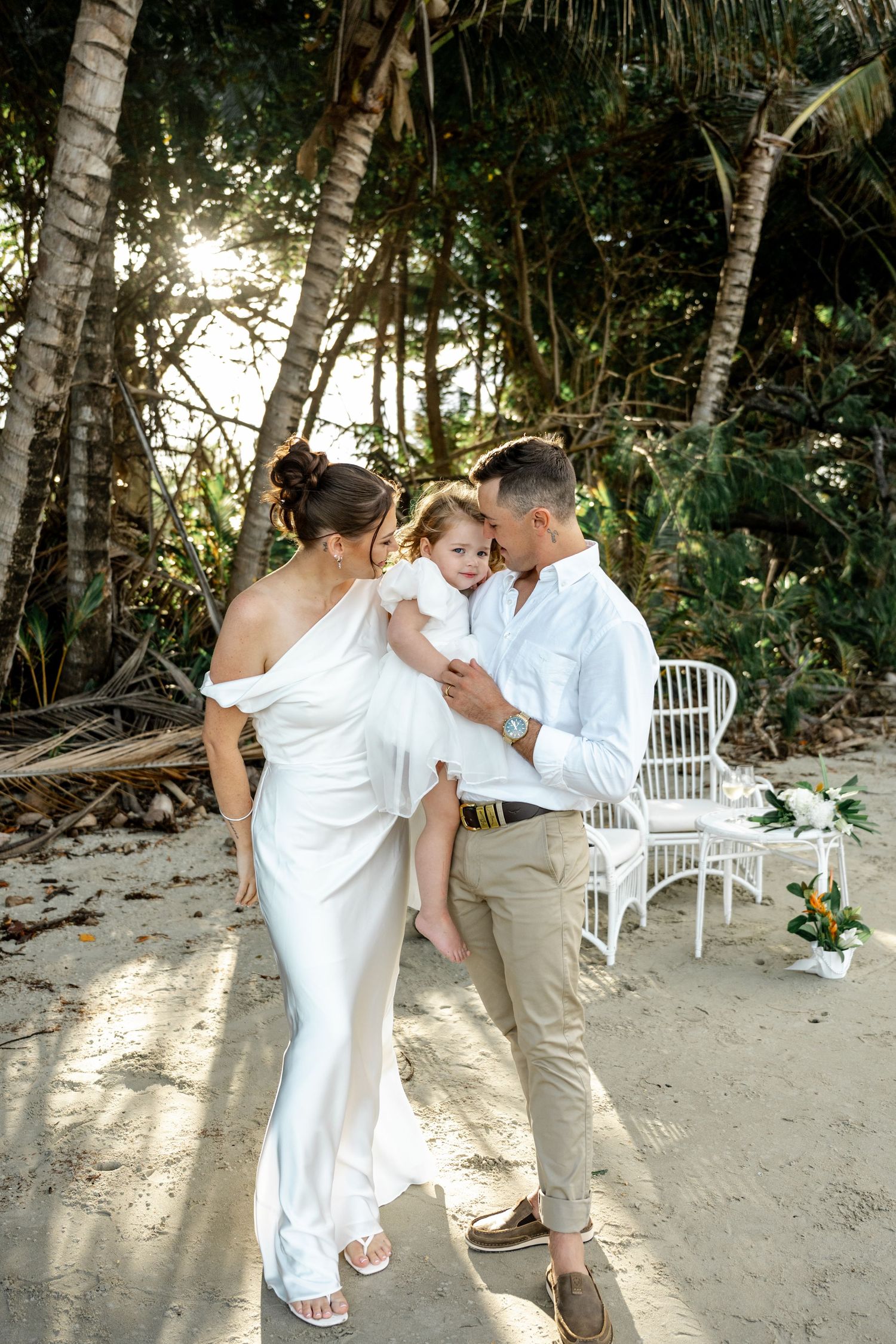 Bride and groom sharing a tender moment with their young daughter on a tropical beach at Four Mile Beach, Port Douglas.