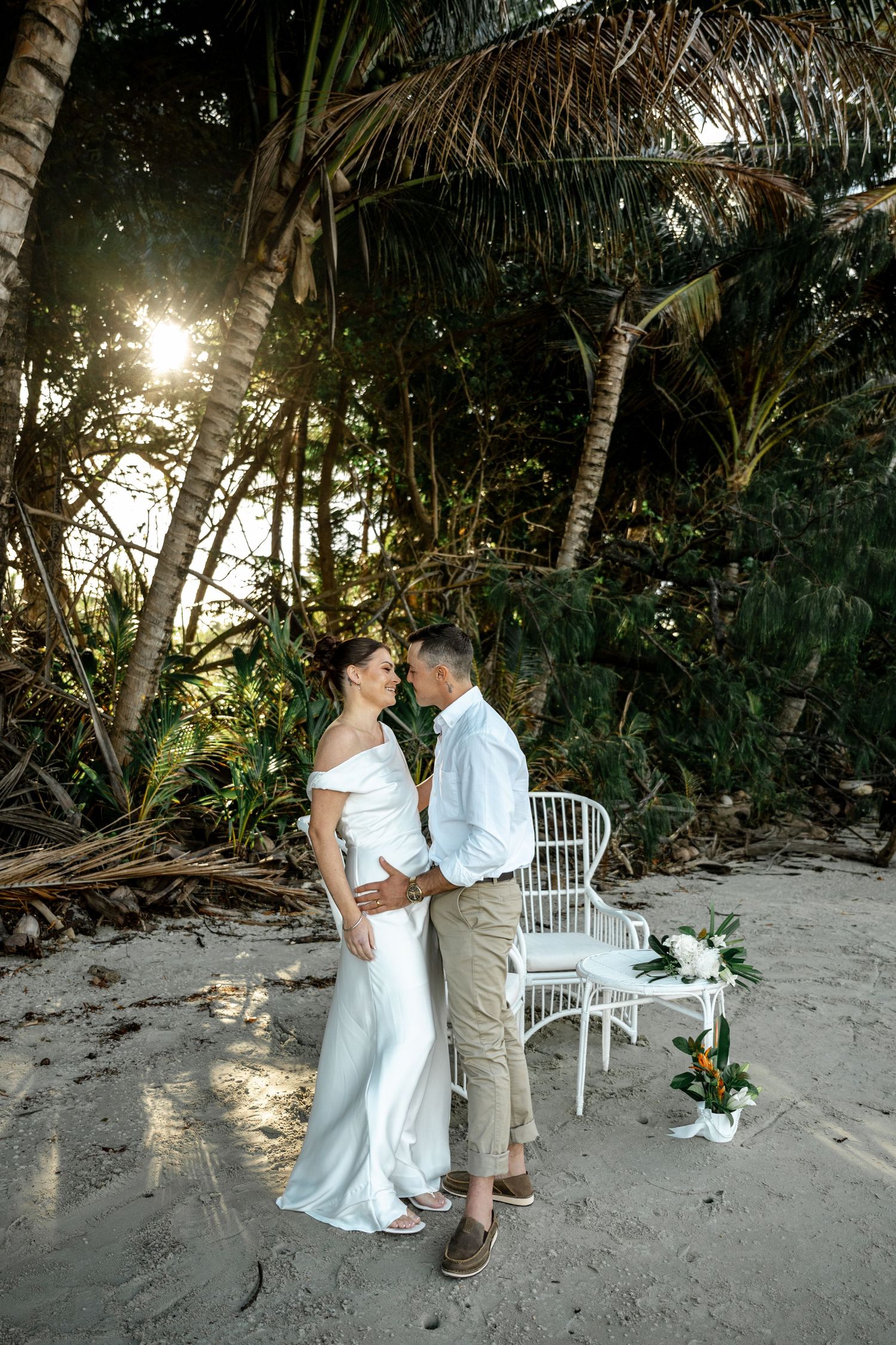 Bride and groom embracing on sandy beach surrounded by lush tropical palm trees at Four Mile Beach, Port Douglas.