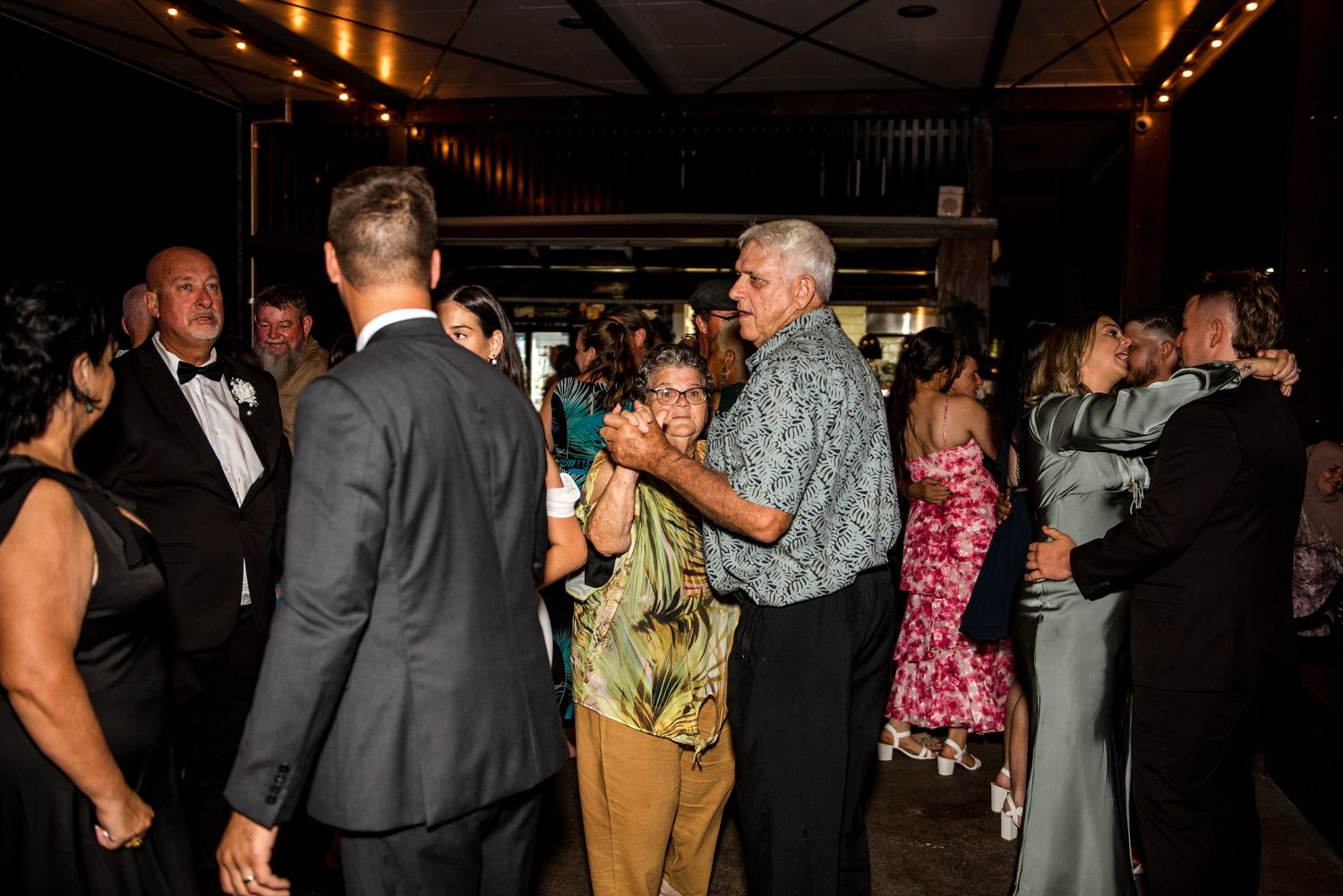 Wedding guests of all ages dance together at a lively evening wedding reception celebration.