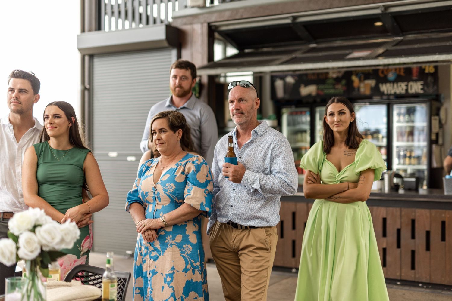 Elegantly dressed wedding guests standing outdoors at a waterfront venue during a reception.