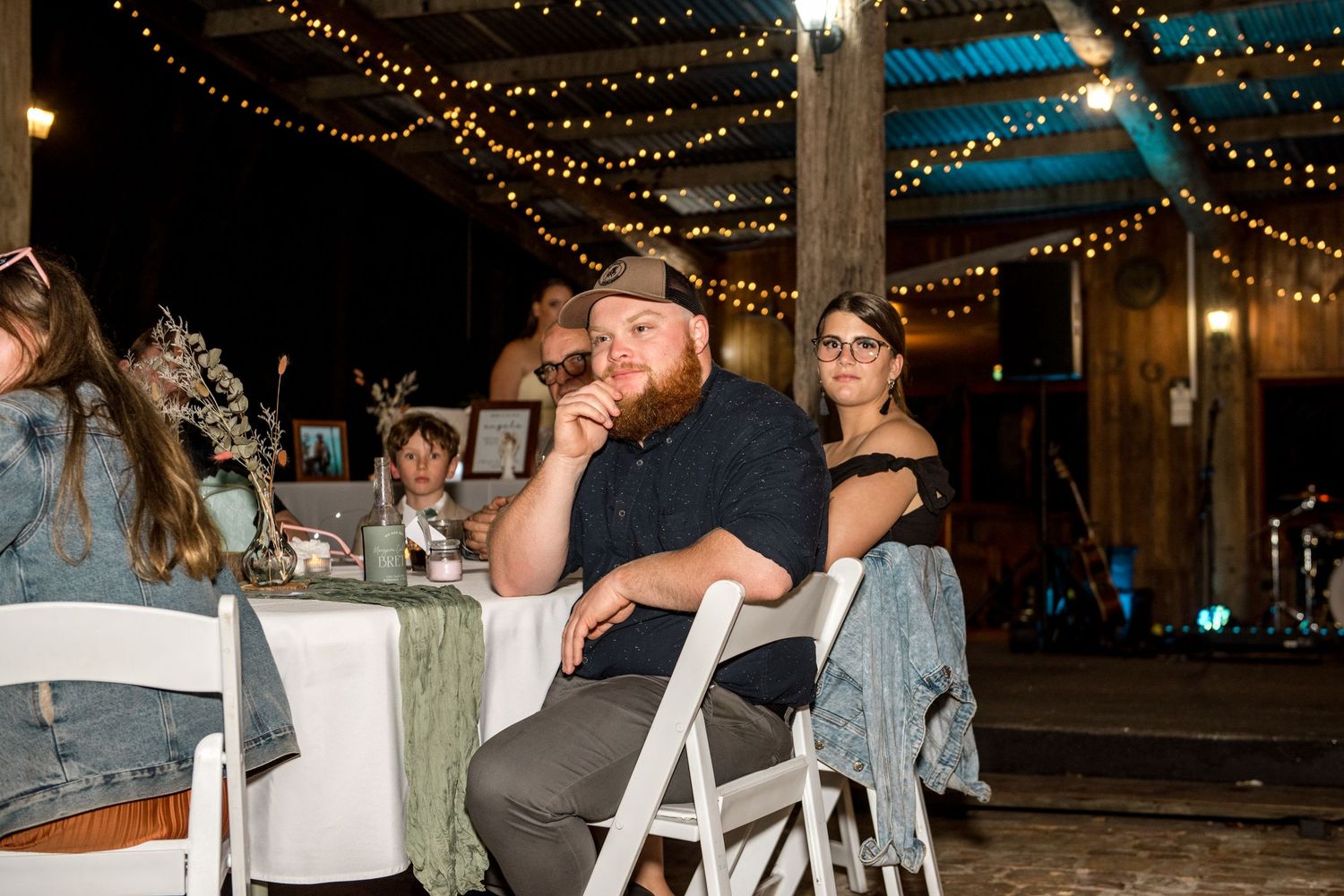Guests seated at decorated tables during an outdoor evening wedding reception with string lights overhead.