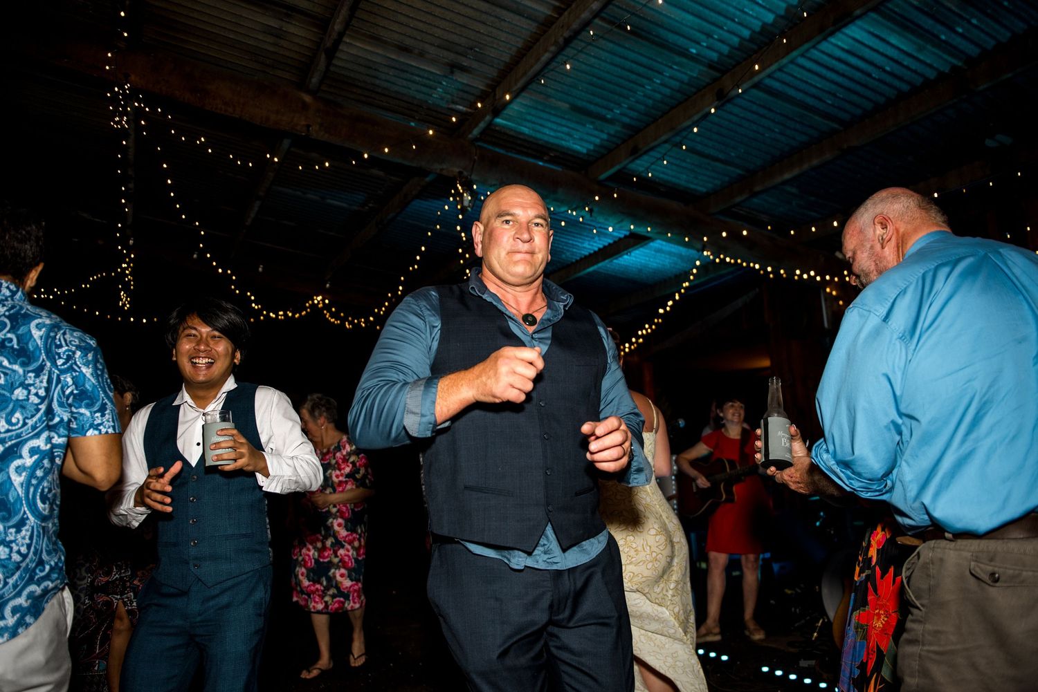 Guests dancing and celebrating joyfully at an evening wedding reception with string lights.