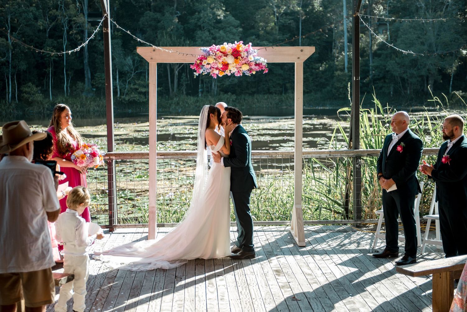 Couple kissing at floral arch during outdoor wedding ceremony.