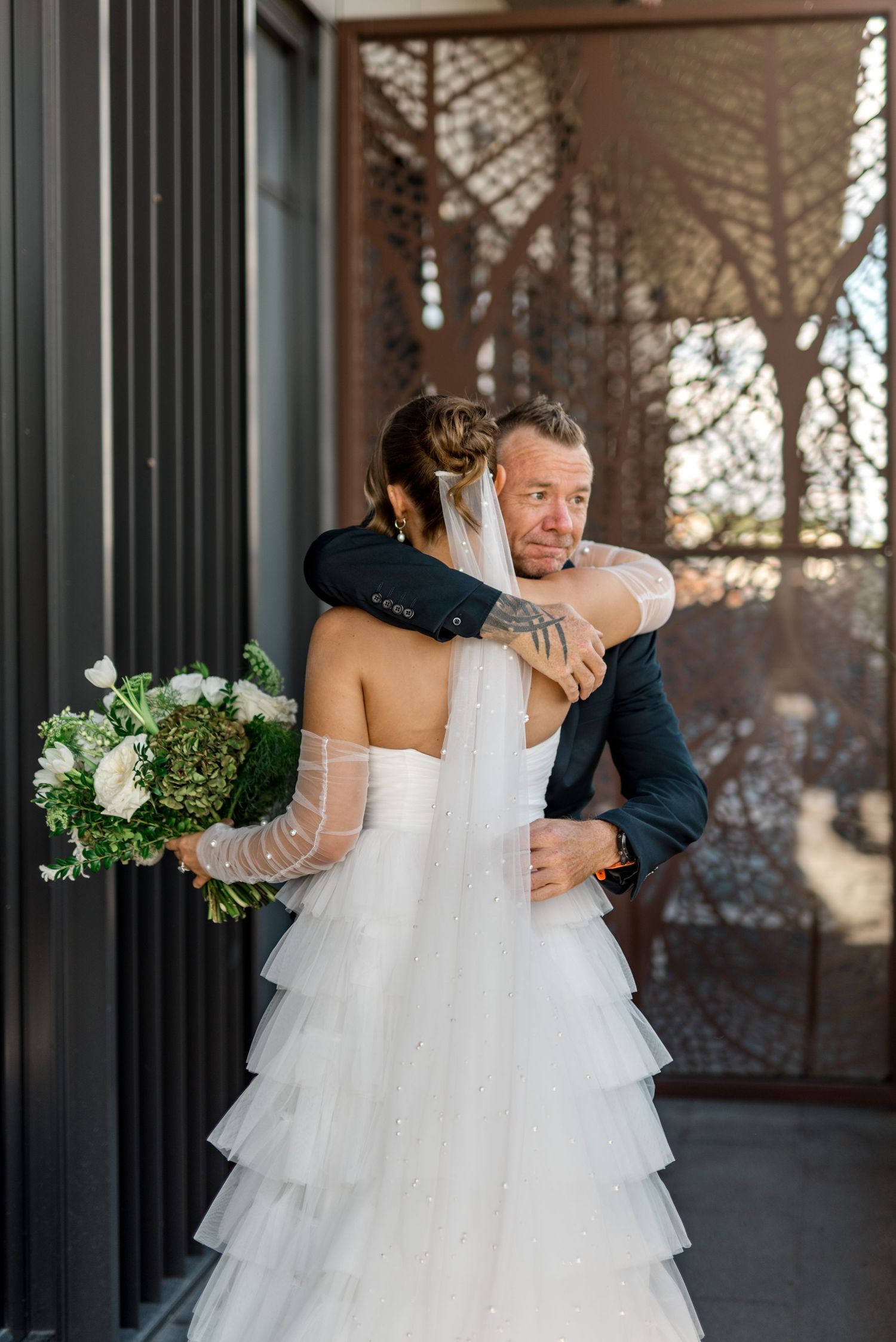 Emotional groom embraces bride in tiered tulle gown during first look at wedding venue.