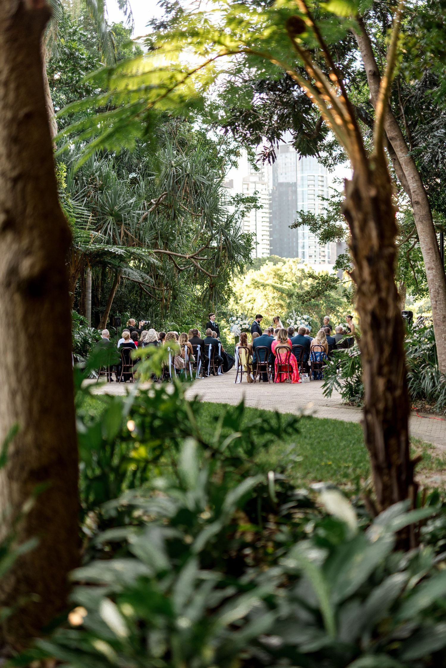 Guests seated at outdoor garden wedding ceremony surrounded by lush tropical greenery.